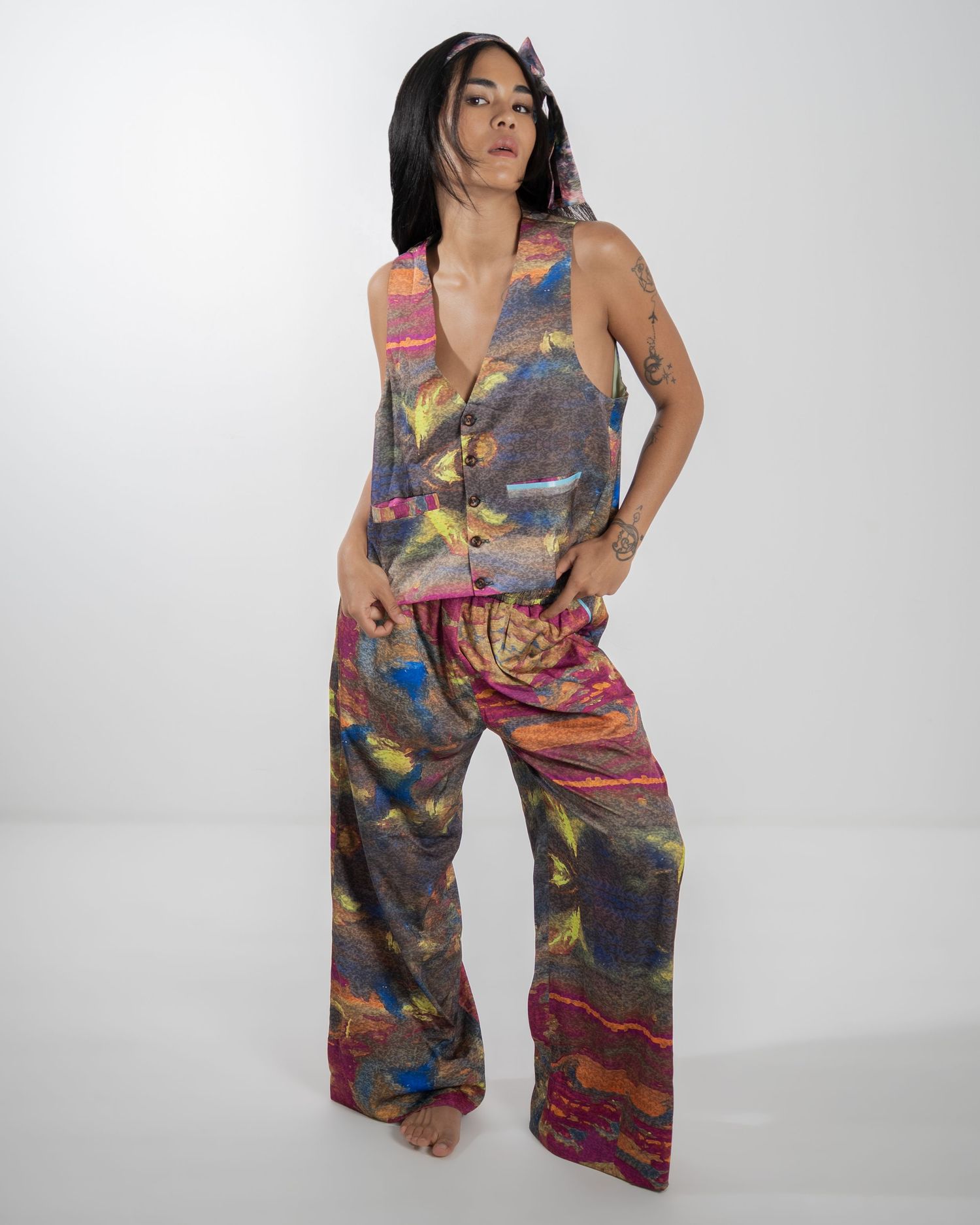Woman poses in a vibrant tie-dye jumpsuit with wide legs and sleeveless design against a light studio background.