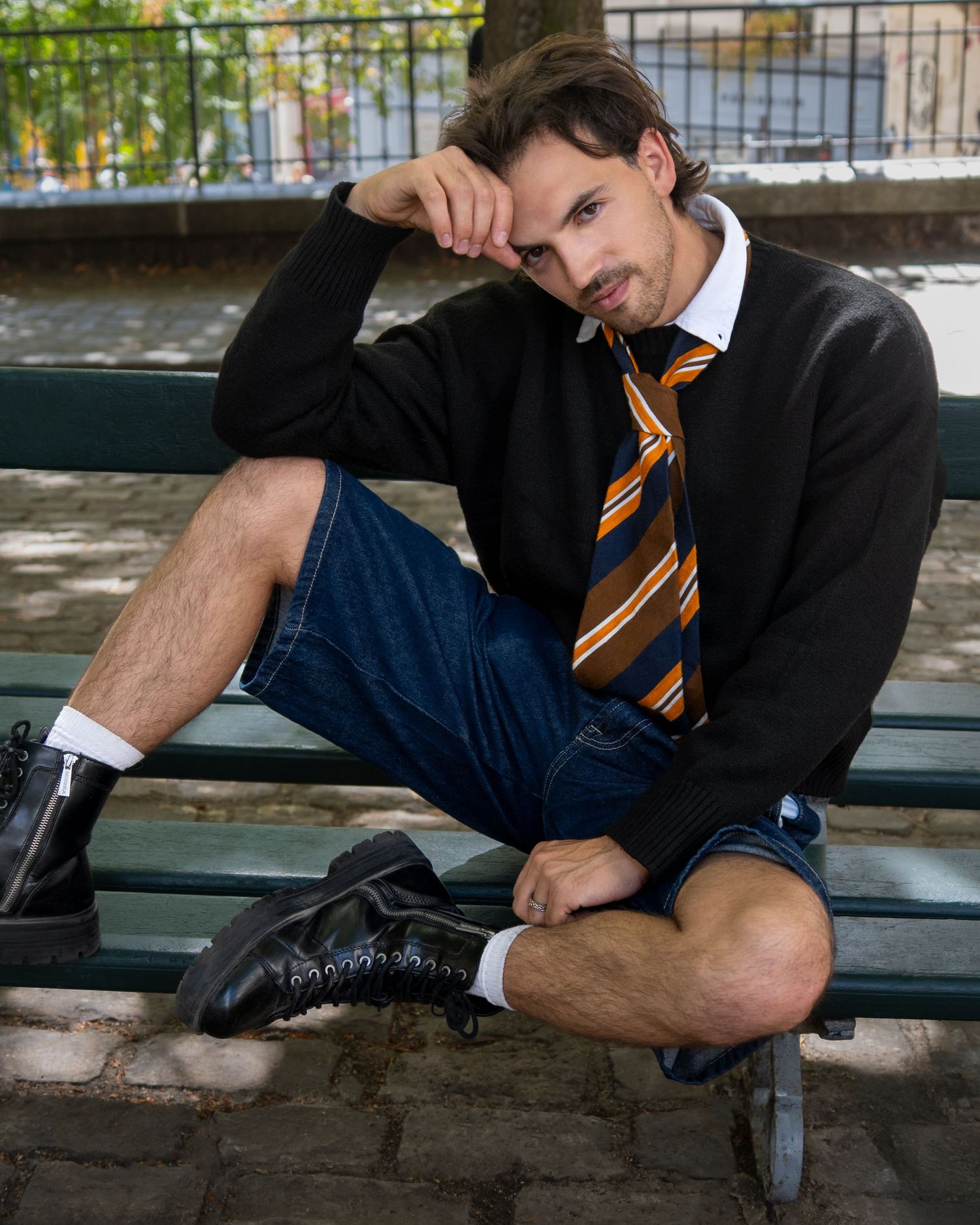 Person in business attire stretches out relaxed on bench wearing striped tie and black suit jacket.