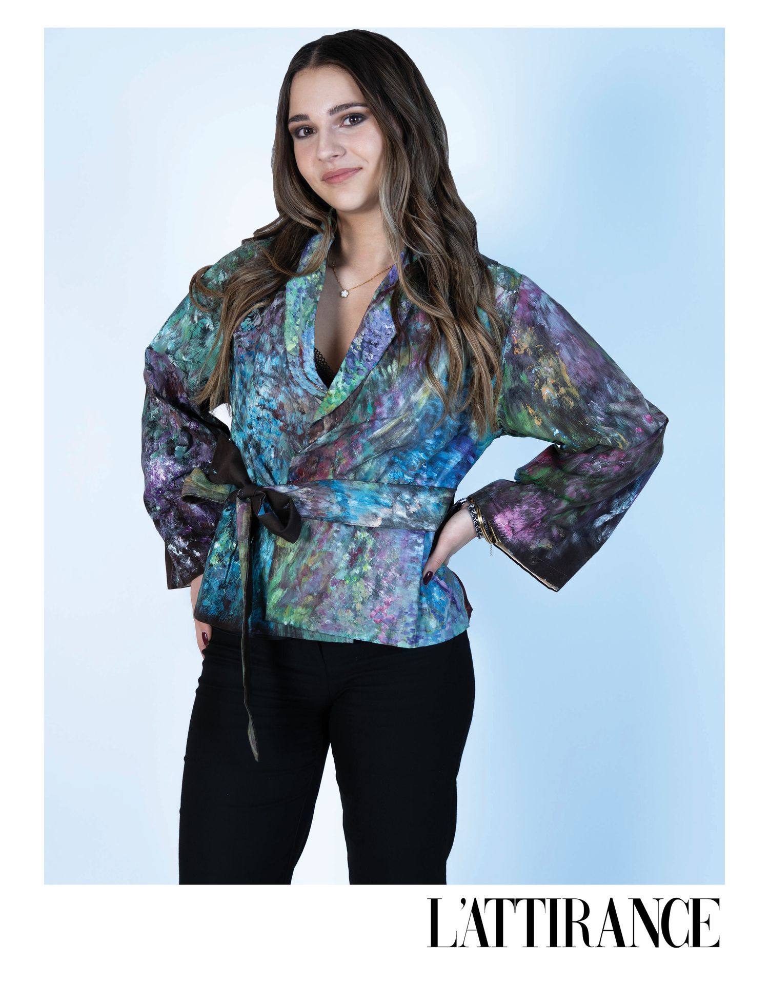 Photographie d'un modèle portant une veste portefeuille à imprimé floral bleu et violet vif avec un pantalon noir sur fond bleu clair.