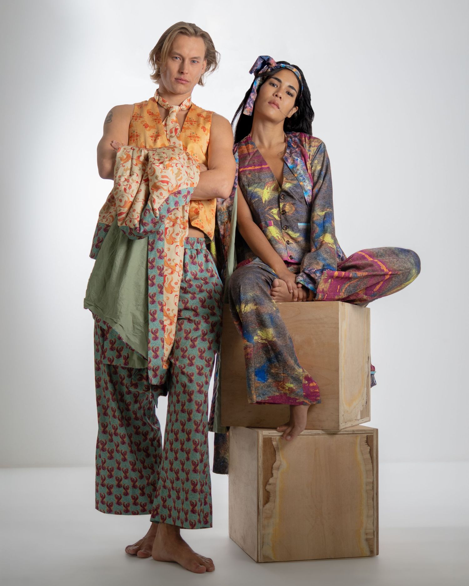 Two models pose together in eclectic patterned outfits against a light background while showcasing sustainable fashion.