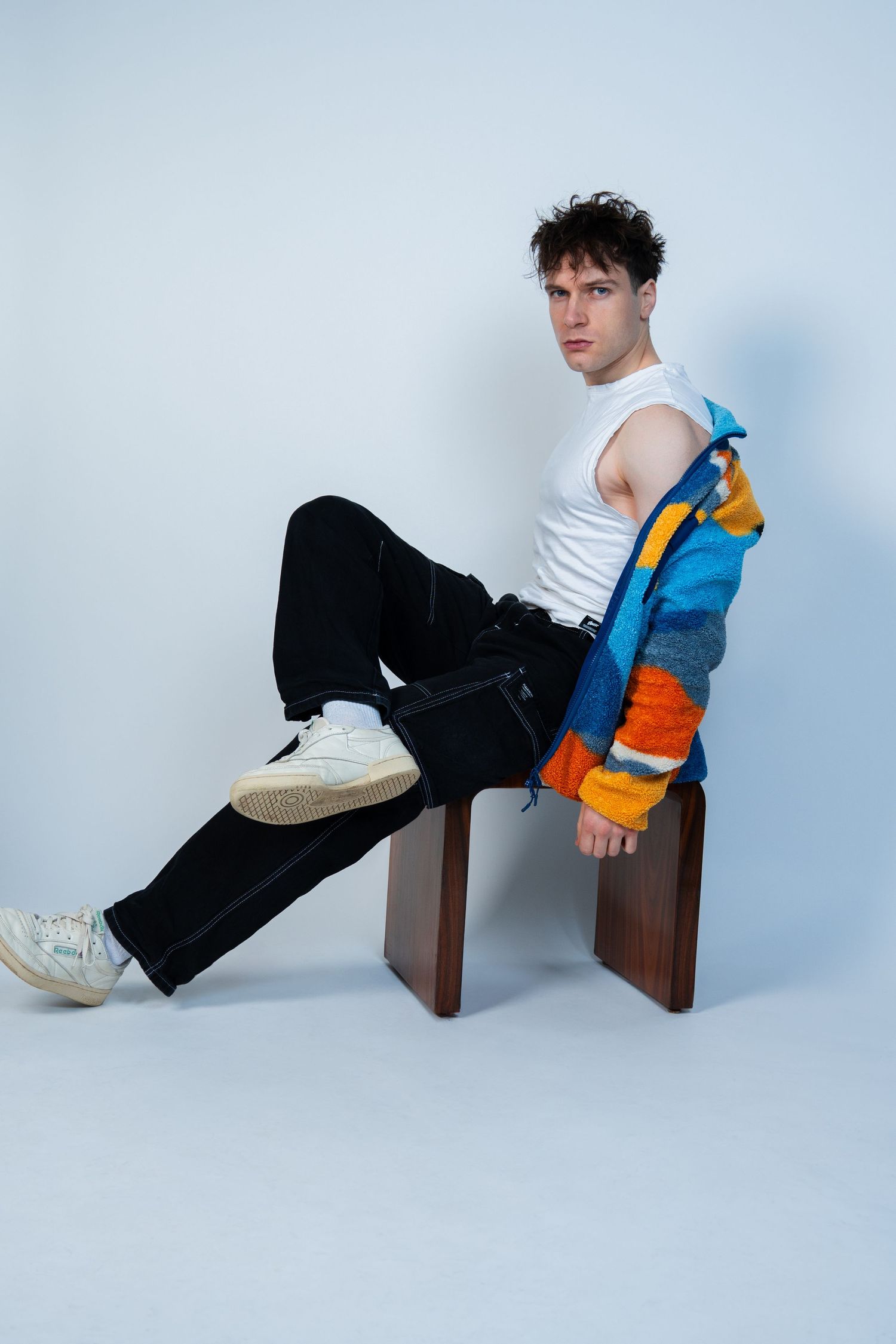 Prise de vue en studio d'un mannequin portant un débardeur blanc et une veste à rayures colorées sur un banc en bois.
