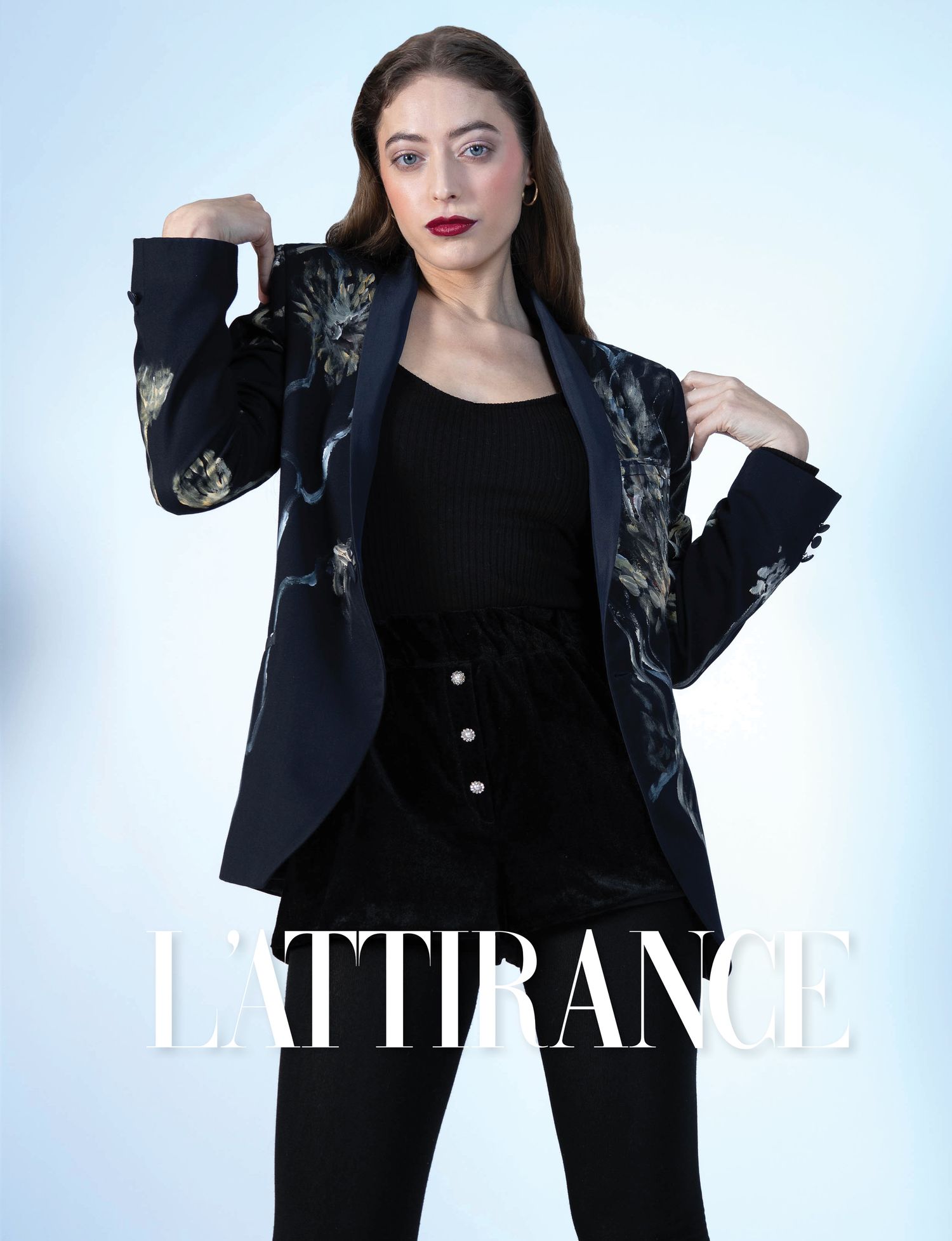 Photographie d'un Modèle en blazer noir avec détails métalliques et pantalon boutonné sur fond blanc pour le magazine L'ATTIRANCE.
