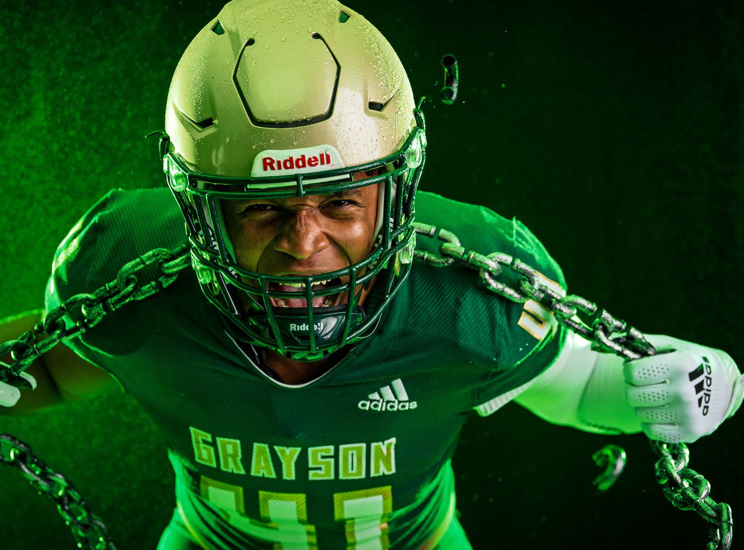 Football player wearing neon green uniform and helmet poses dramatically against dark background with matching green lighting.