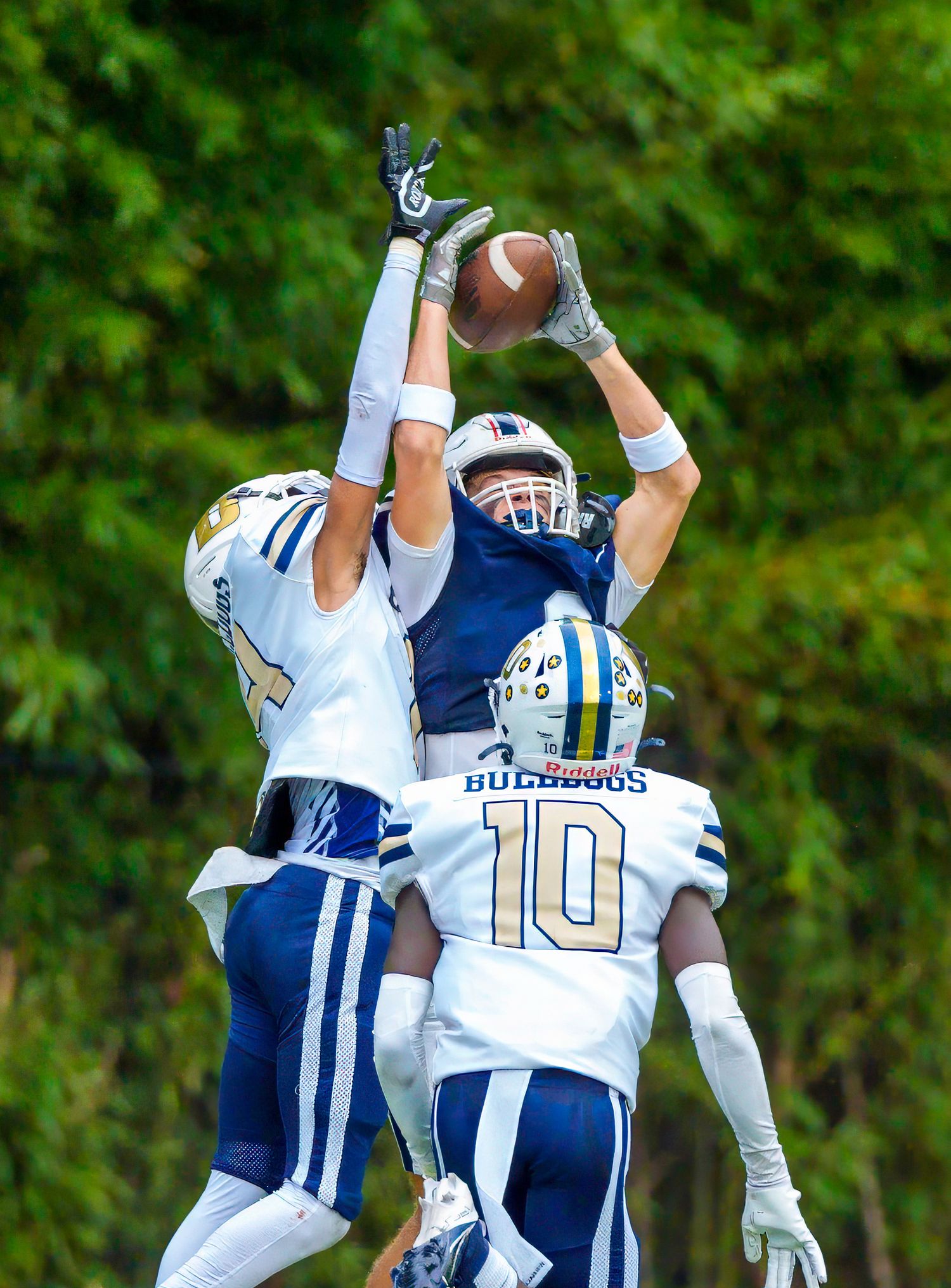 Football players jumping for the ball in a competitive play wearing blue and white uniforms.