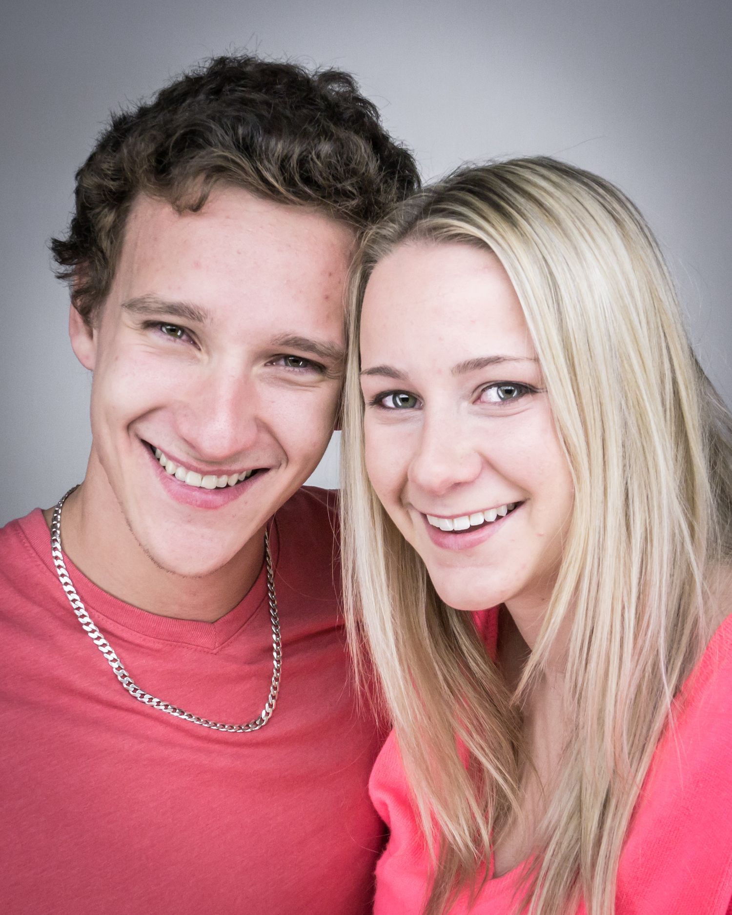 Close-up portrait of a couple wearing matching coral tops smiling at camera.