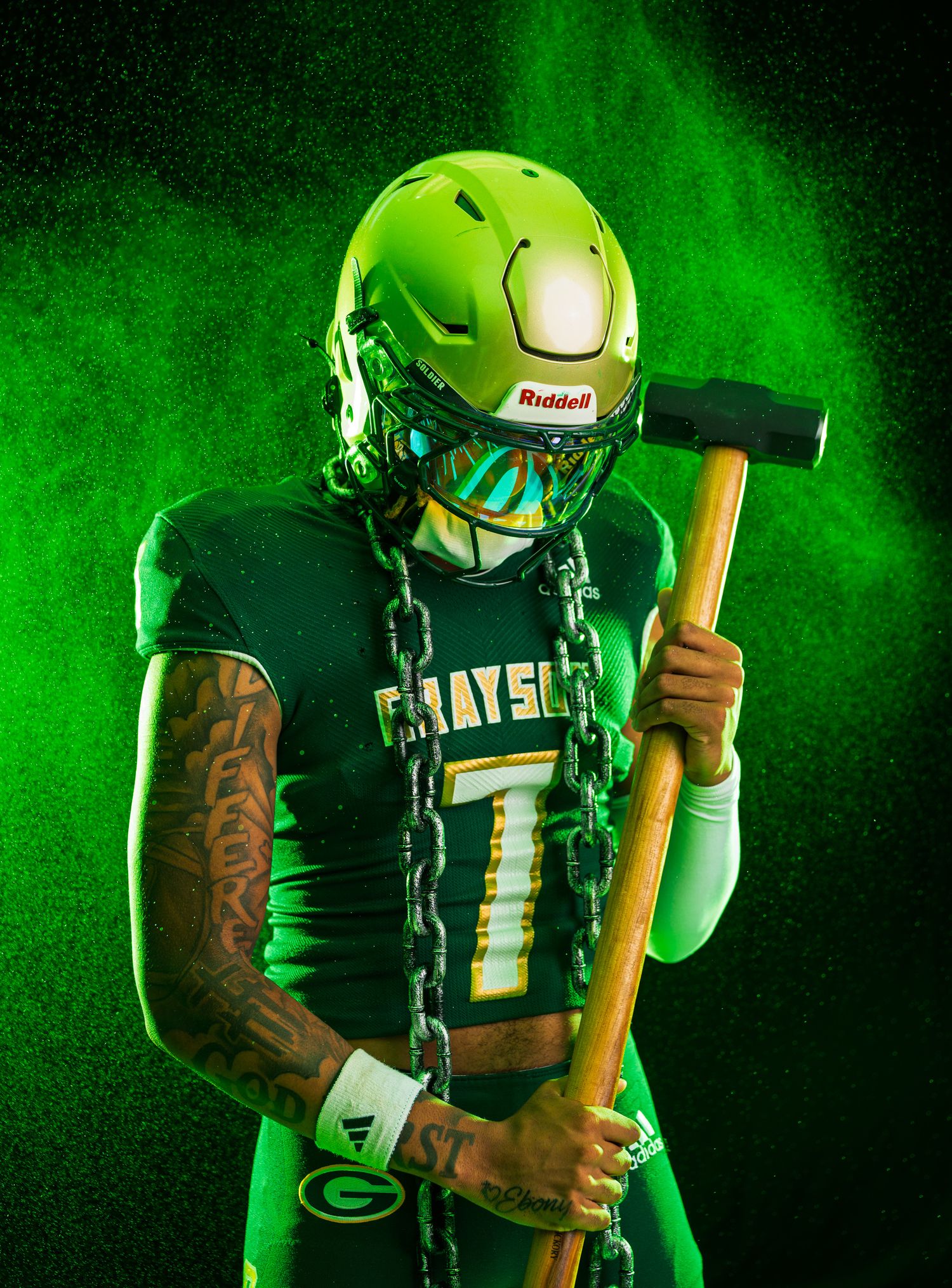 Football player in black uniform holding a wooden baseball bat against dramatic green-lit smoky background effect.