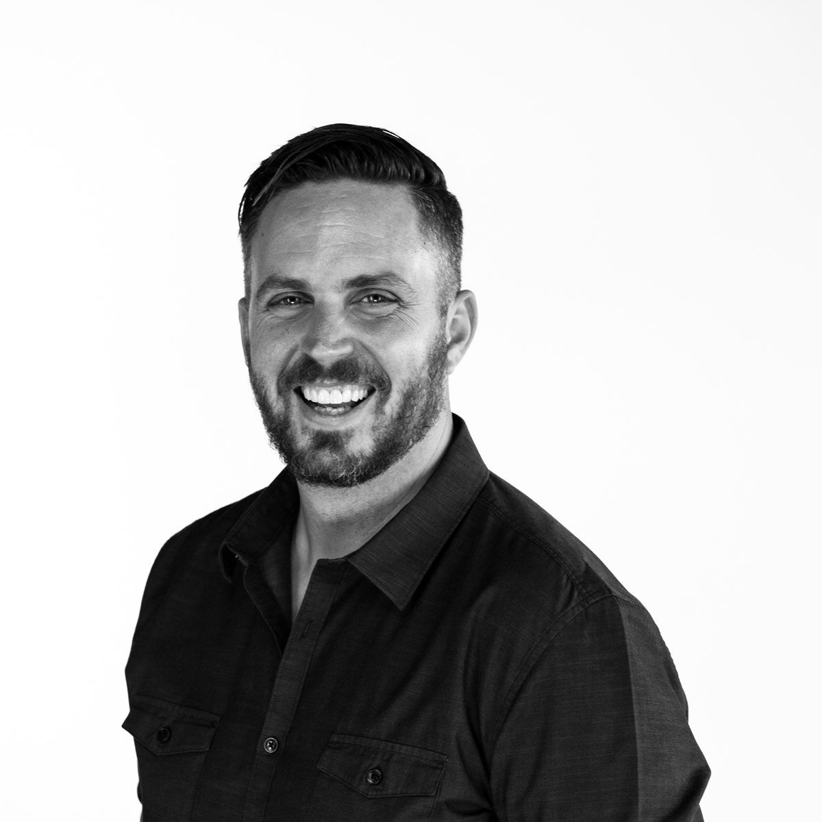 Professional black and white headshot of person in dark shirt smiling at camera.