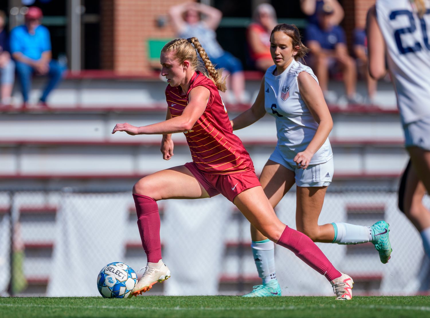 Soccer player in red uniform dribbles ball during competitive match against opponent in light blue.