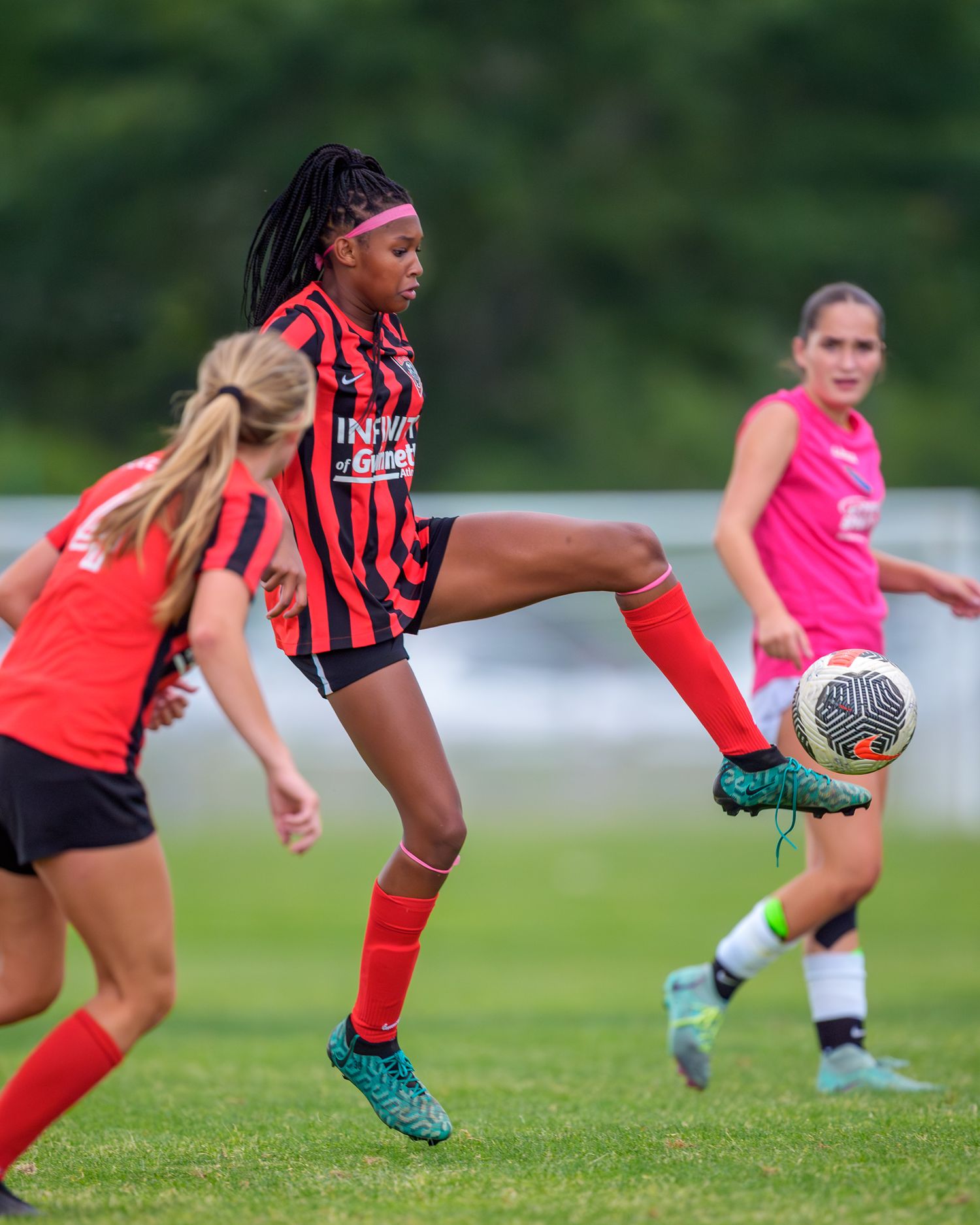 Soccer player in black and red striped uniform performs high kick with ball during match.