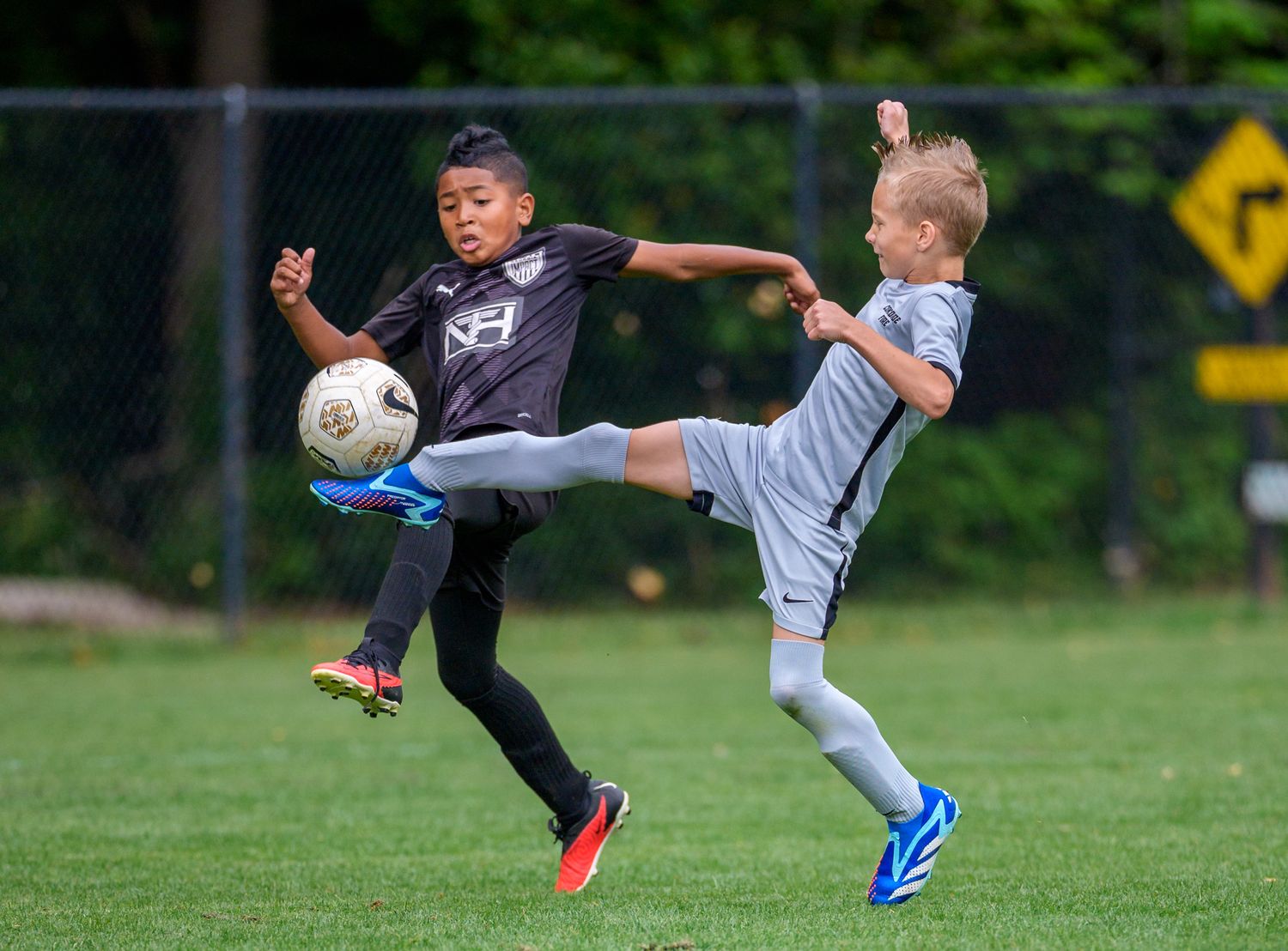 Two youth soccer players battle for possession of the ball with simultaneous kicks.