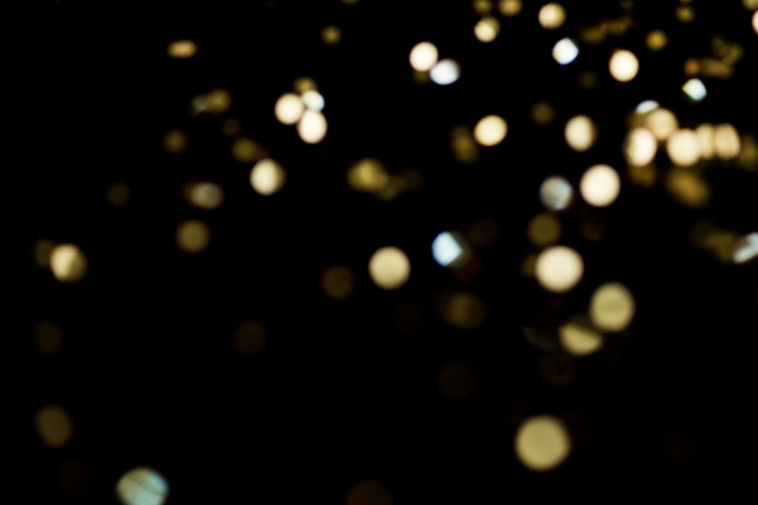 Golden bokeh lights glowing against a dark black background, creating a dreamy festive sparkle effect.
