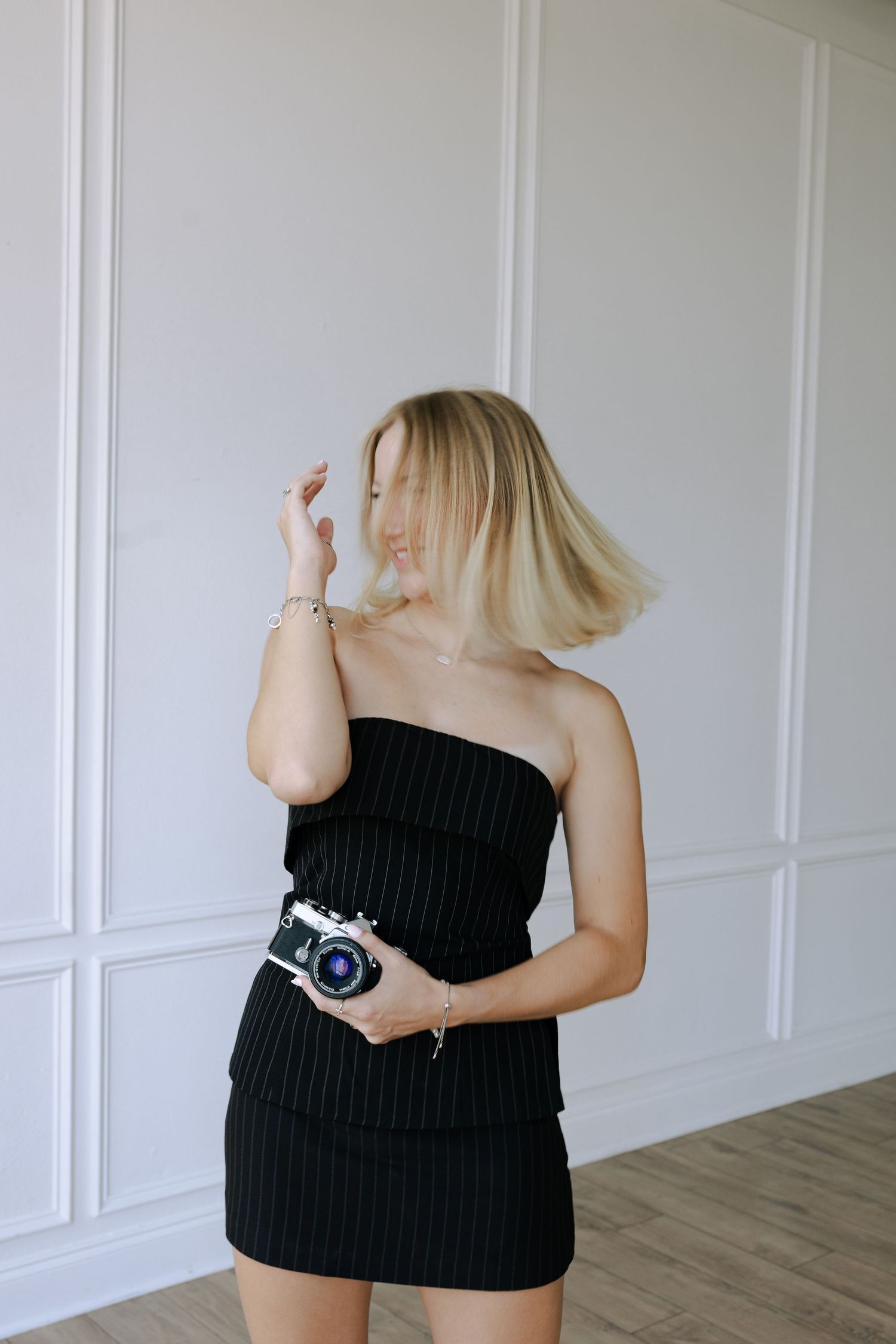 Vintage film camera held in a black strapless dress against white paneled wall interior.