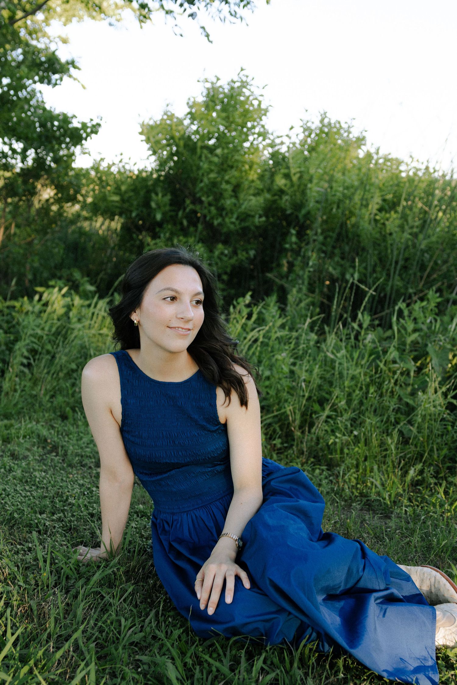 A person in a navy blue dress poses gracefully on grassy ground during an outdoor photo session.