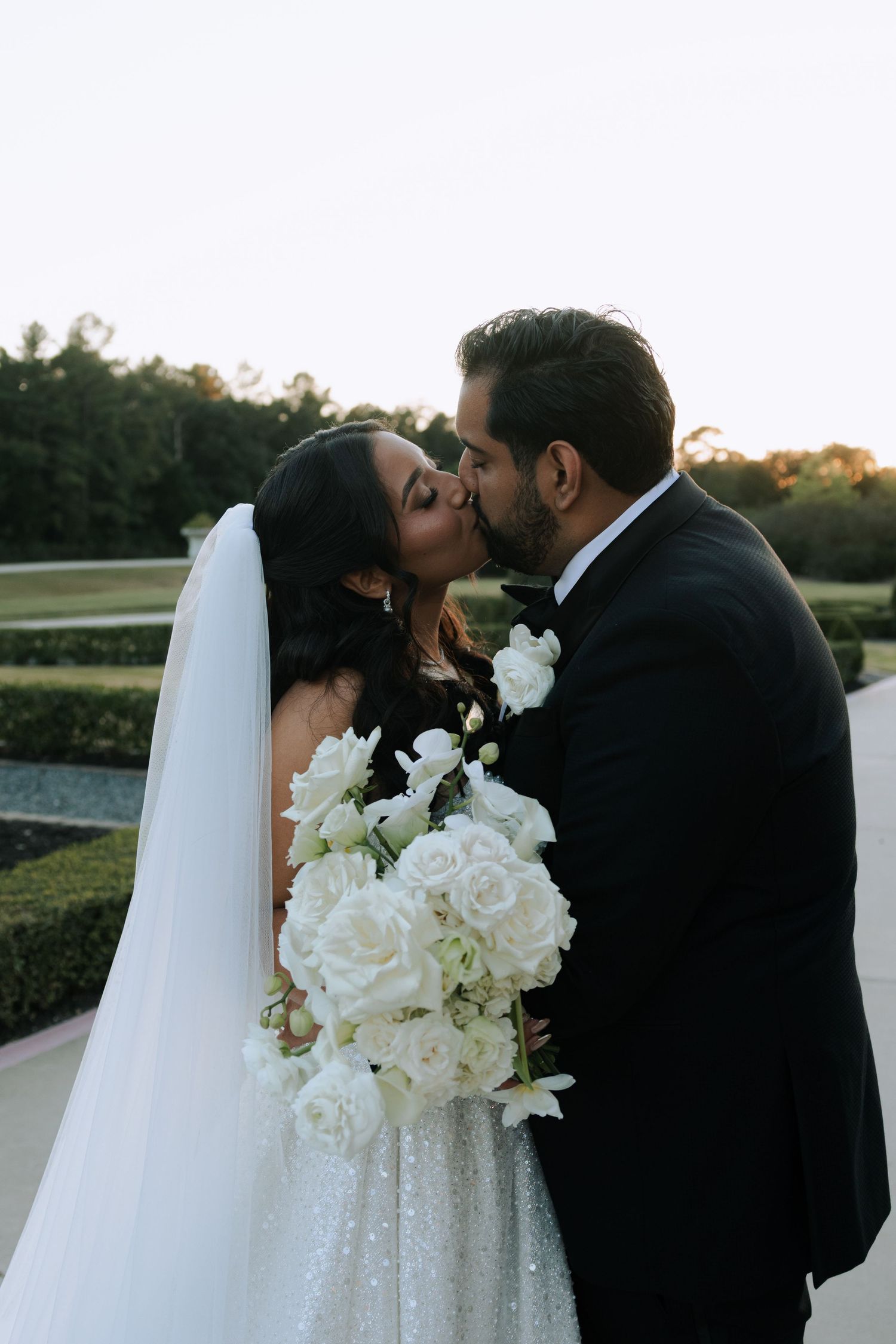 Romantic sunset wedding portraits showing couple sharing intimate moments with white rose bouquet and flowing veil.