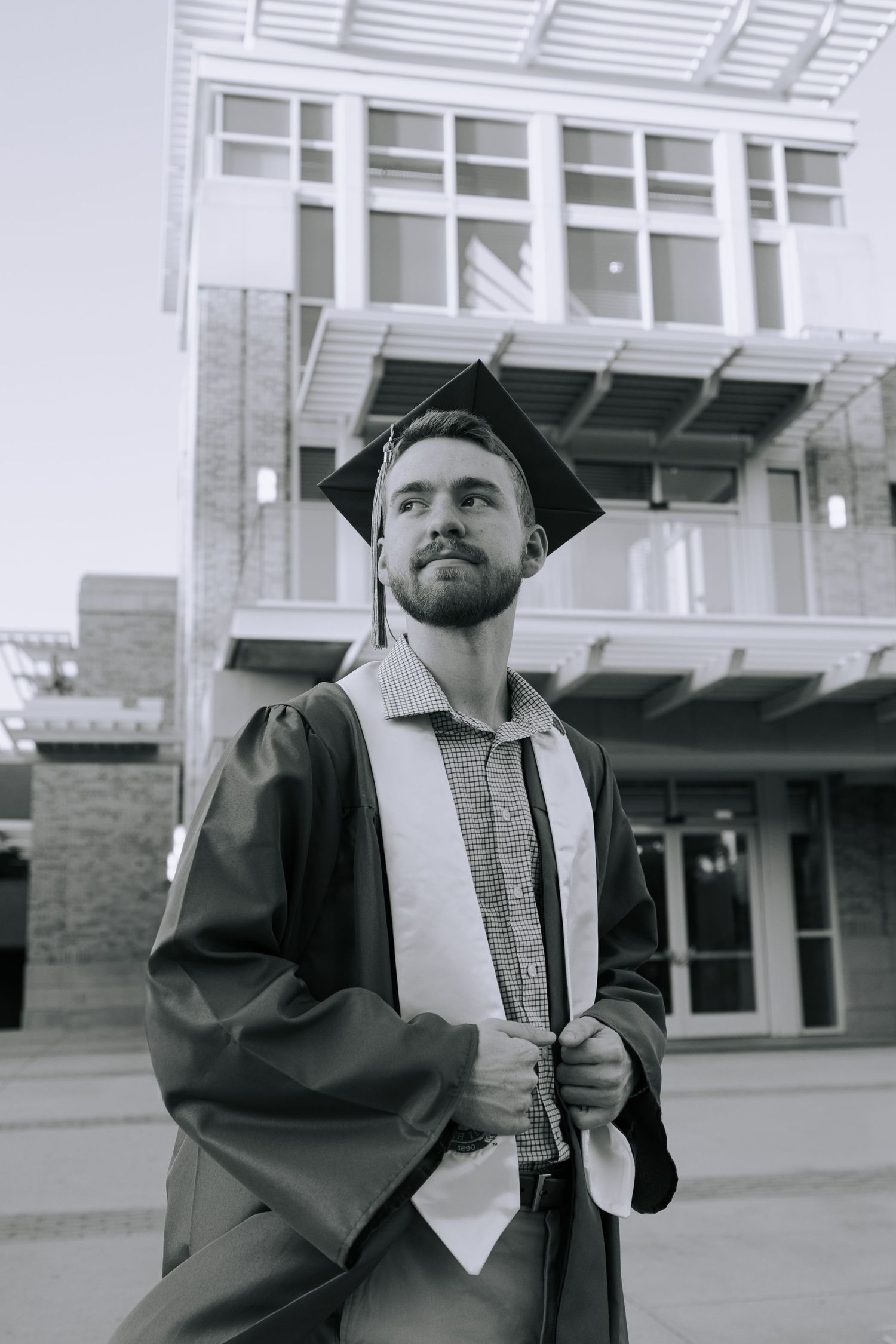 A graduate in cap and gown poses with their diploma on campus in a series of black and white photos.
