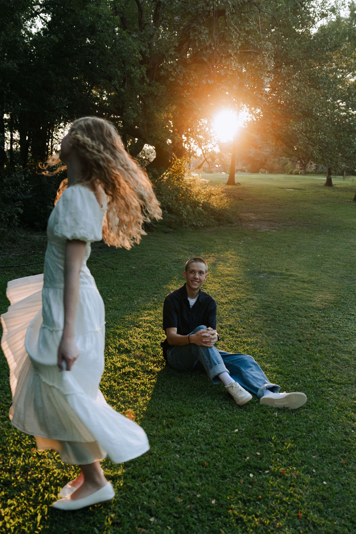 A couple spends time together in a sunlit park with golden light streaming through trees at sunset.