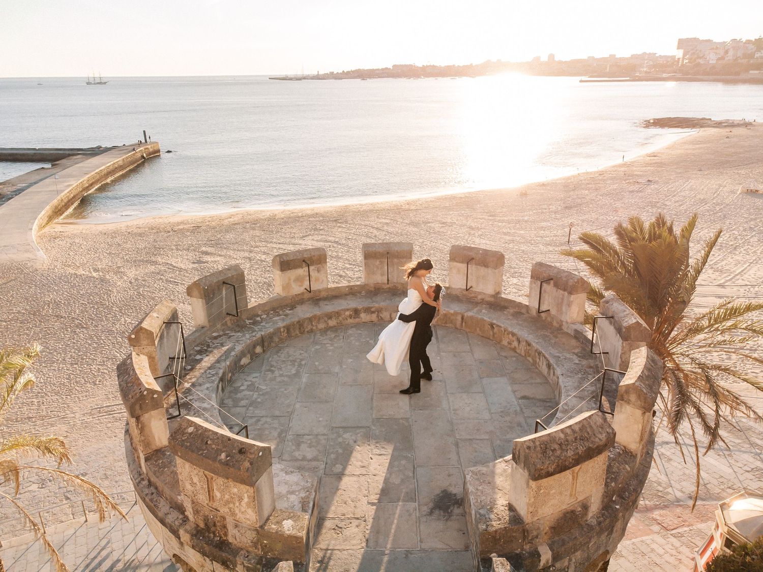 Aerial portrait of bride and groom at Forte da Cruz tower with sunset taken at the coupl´s session, over the sea in Portugal
