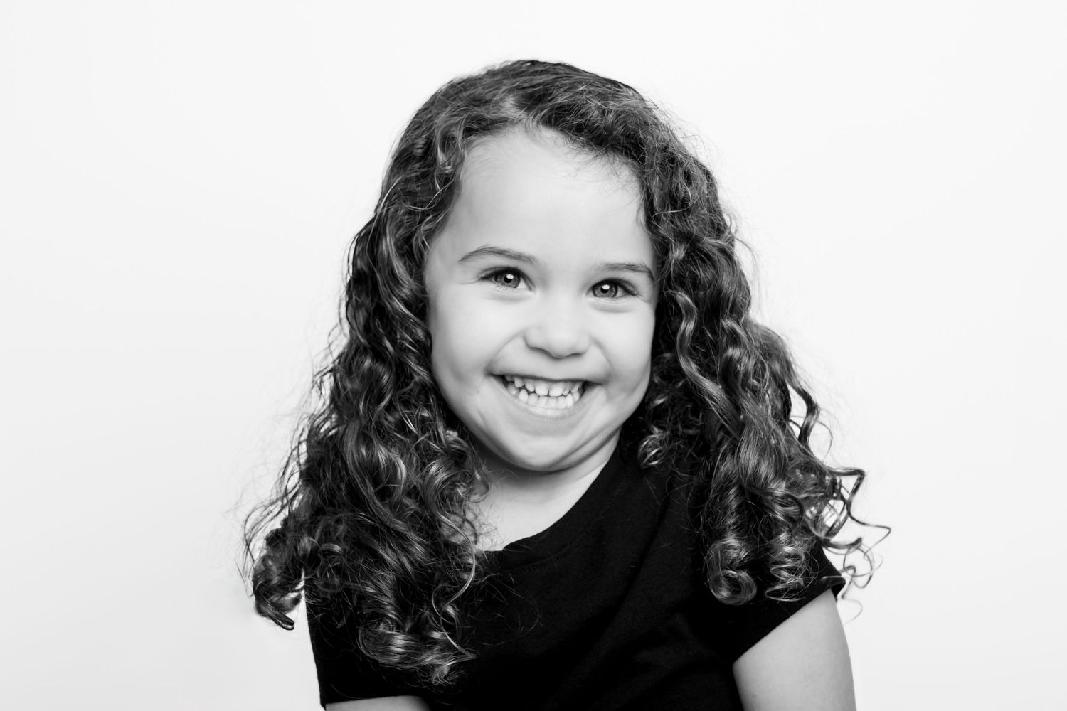 Black and white portrait of a young child with dark curly hair smiling at the camera.