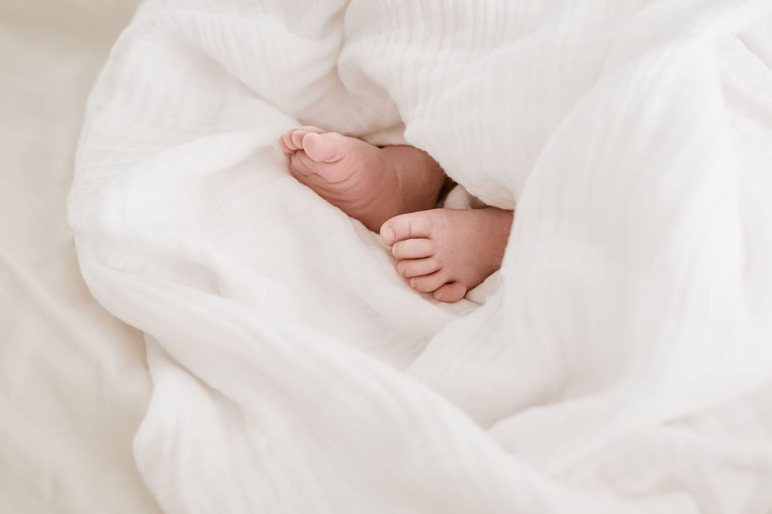 Soft focus images of baby feet and hands wrapped in white cotton fabric.