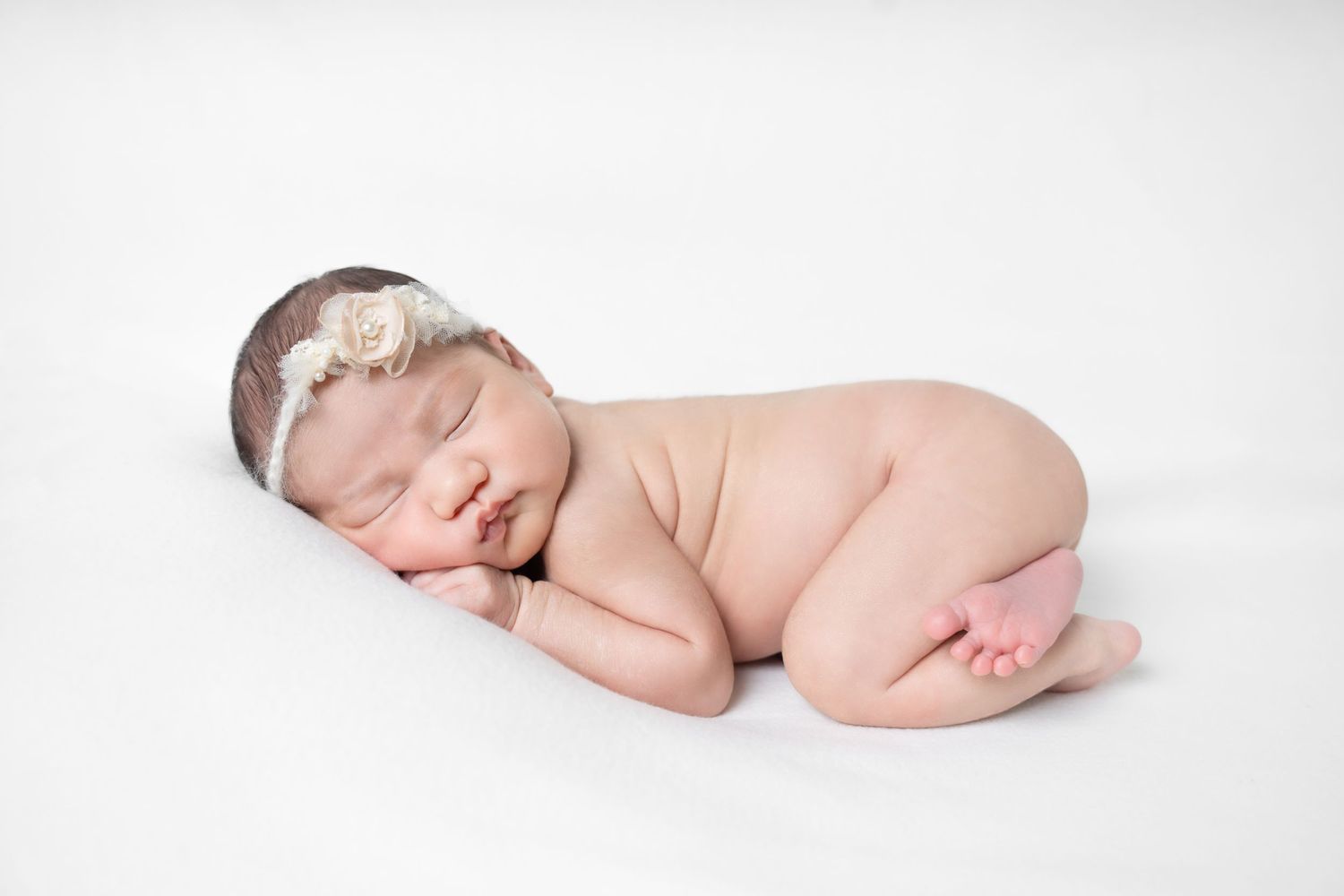 A sleeping newborn baby curled up in a peaceful pose against a white background.