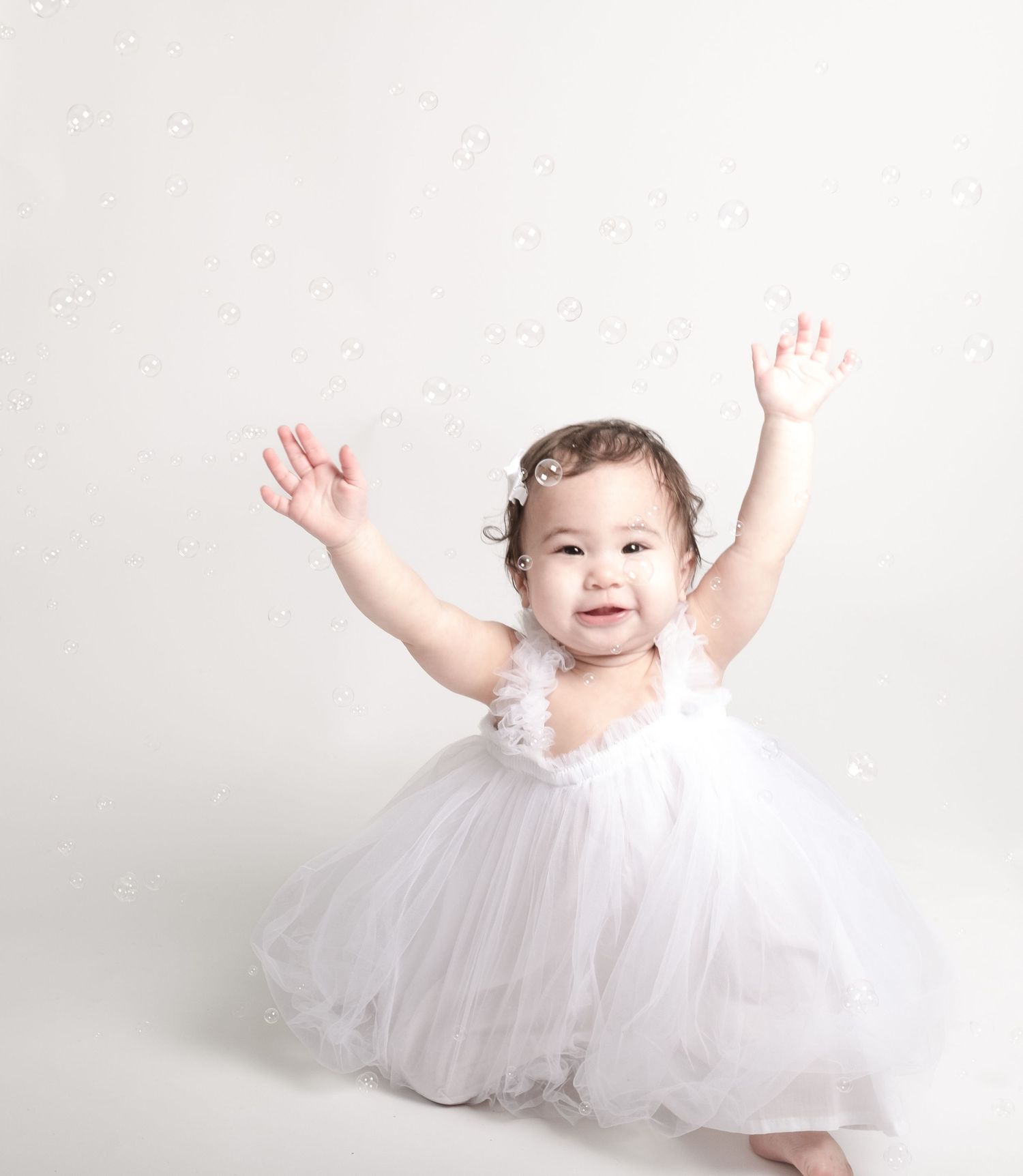 Baby in white tulle dress twirling and playing against white background.