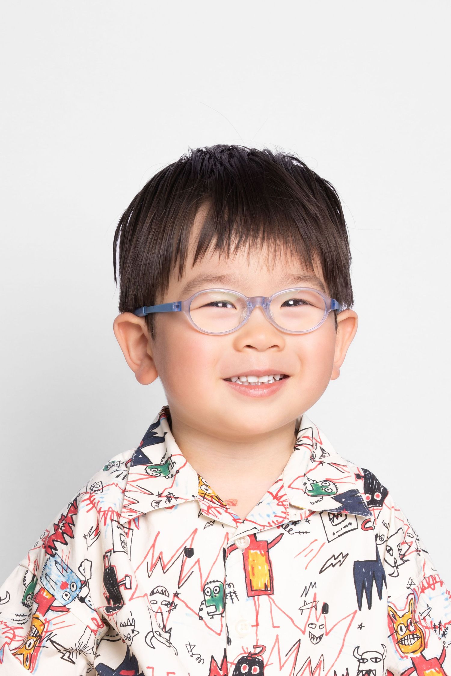 A smiling child wearing glasses and a white patterned hoodie with cartoon illustrations.