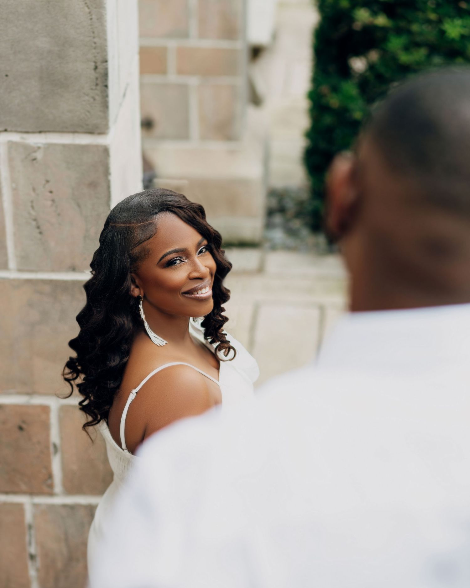 Elegant wedding couple poses against stone columns in an outdoor setting.