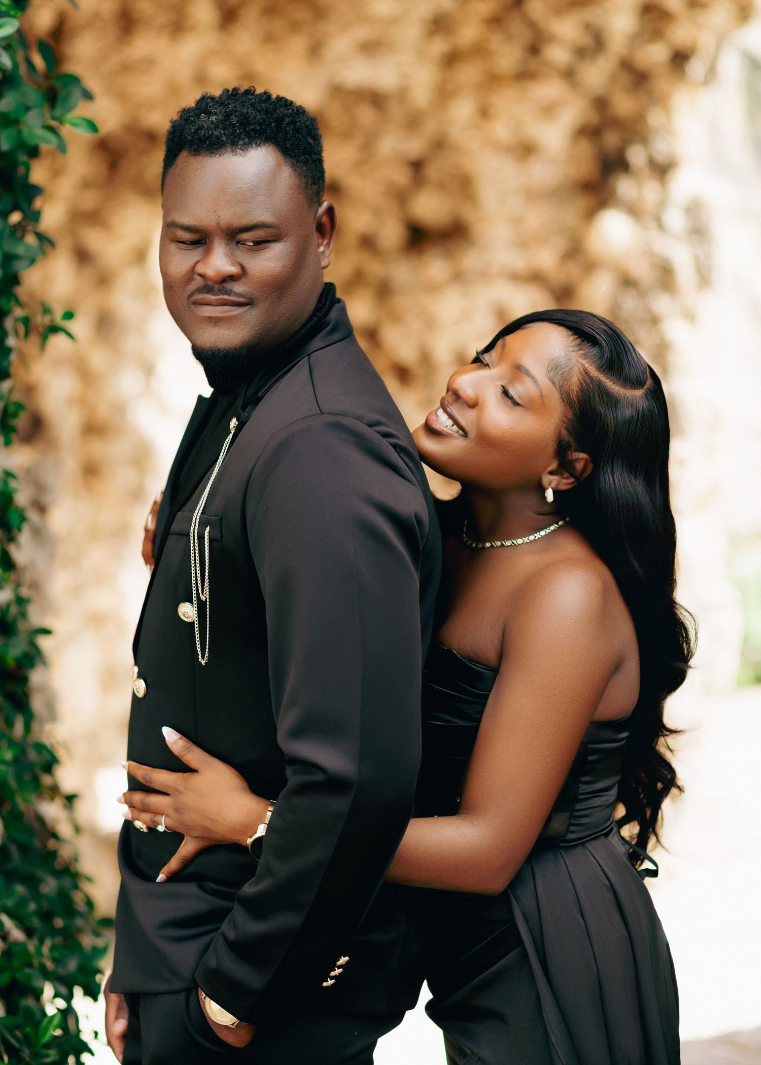 A romantic couple embraces outdoors during a portrait session, with the woman in black hugging from behind.