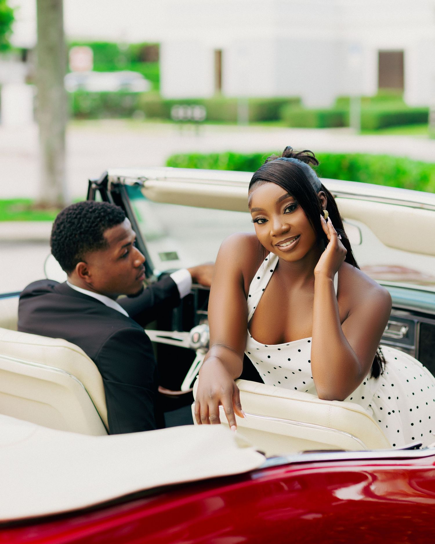 Couple sharing intimate moments while posing with a classic red convertible car.