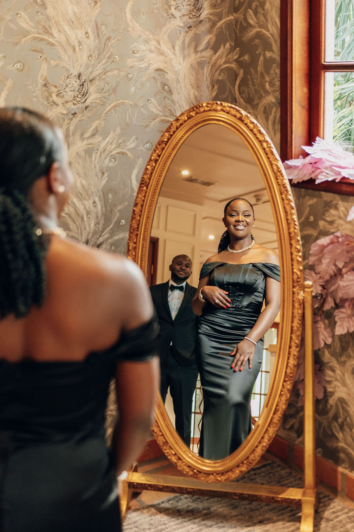 Elegant couple reflected in ornate gold mirror during formal photoshoot.