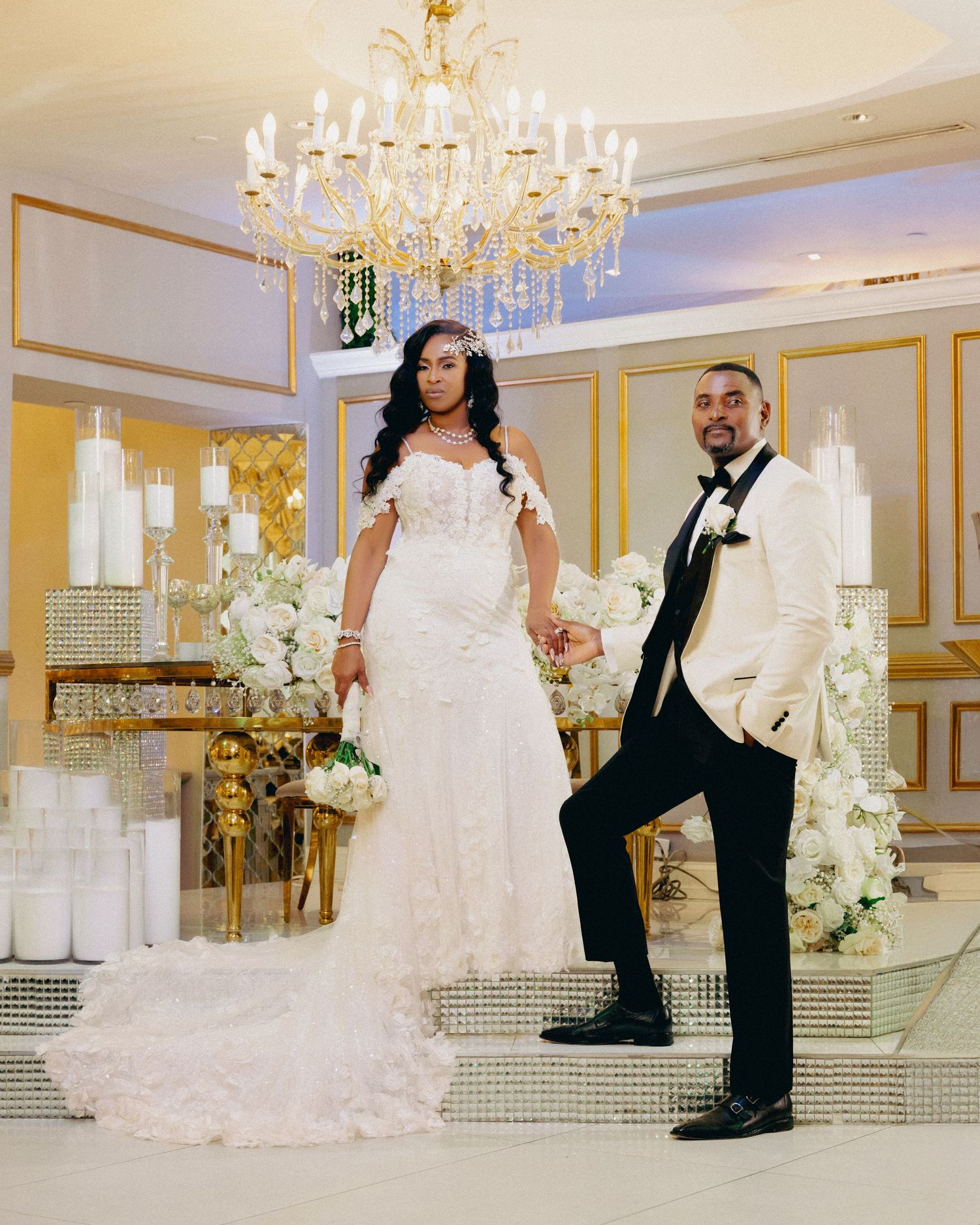 Wedding couple poses in elegant gold-trimmed ballroom with crystal chandeliers.
