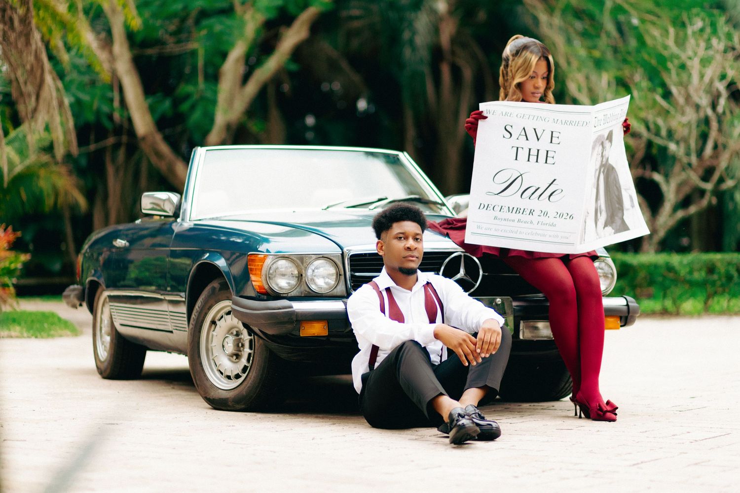 A save the date photo shoot featuring a classic black convertible car and a decorative announcement sign.