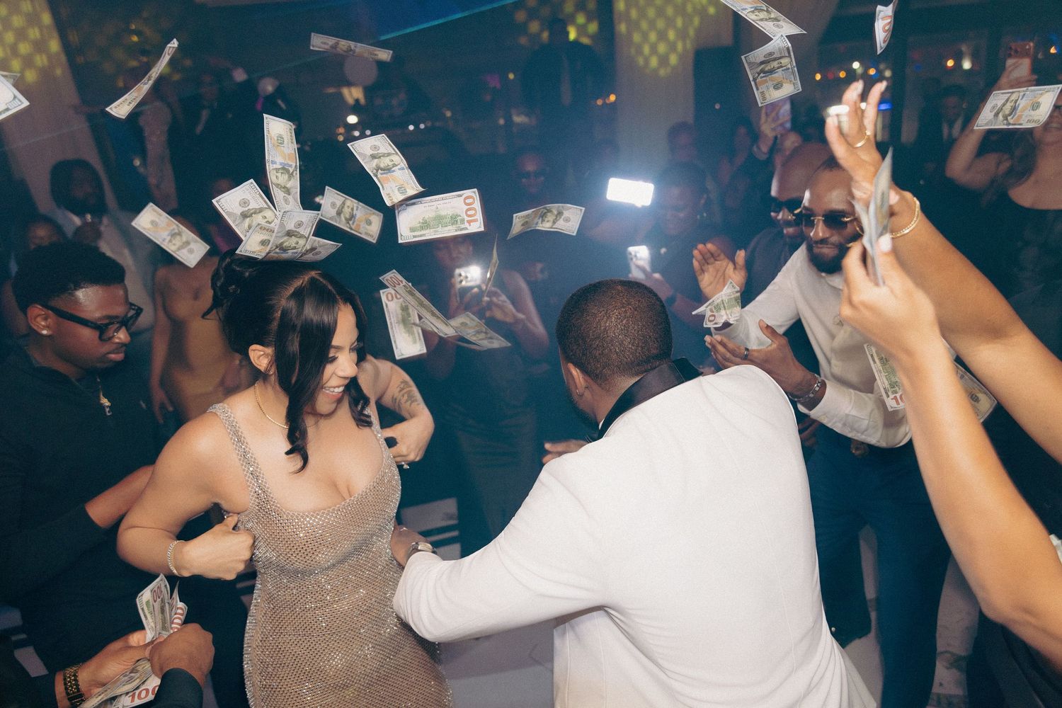 Wedding guests celebrating on dance floor with money raining down at reception party.