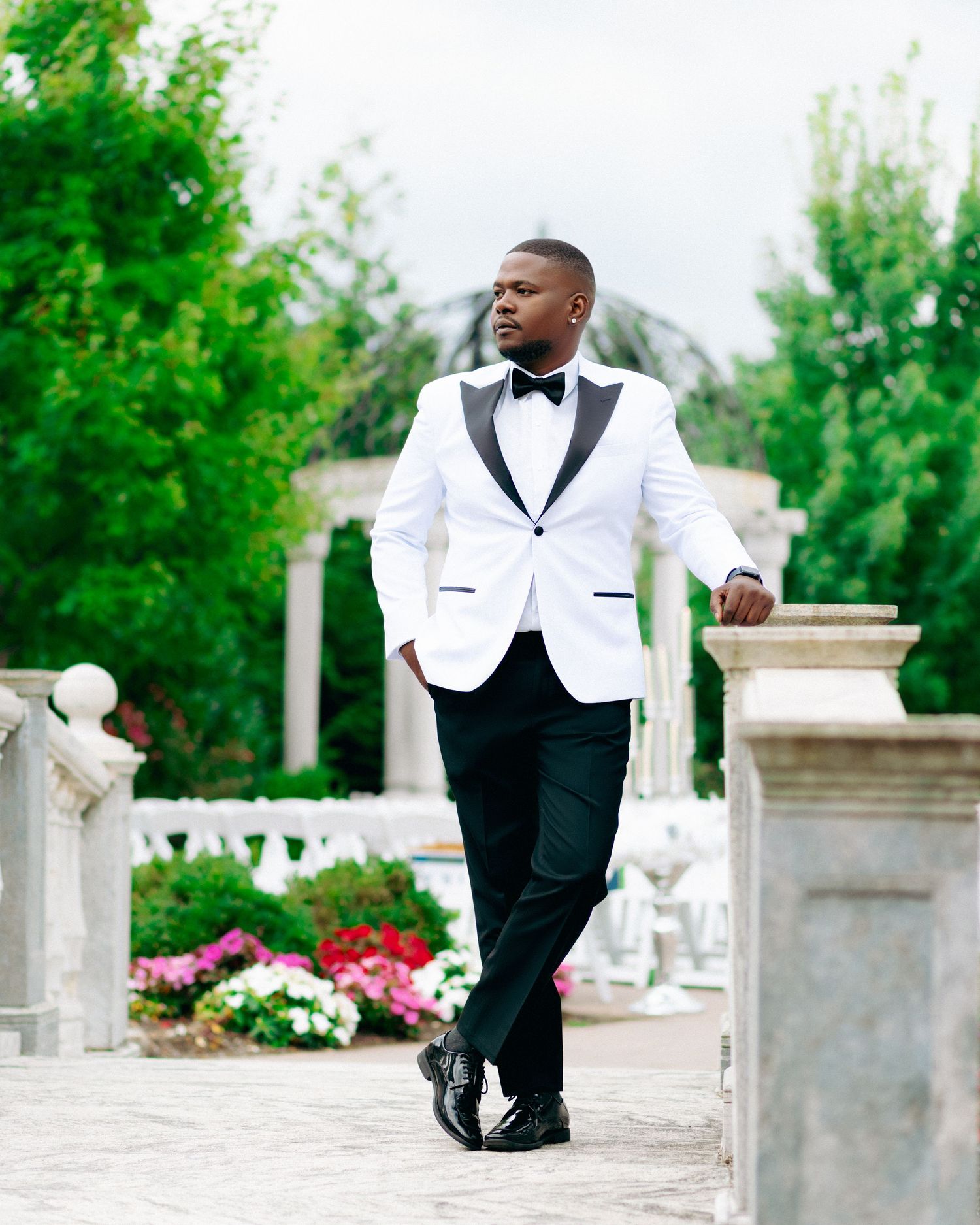 Groomsmen in formal black and white attire posing along stone balustrade at outdoor venue.