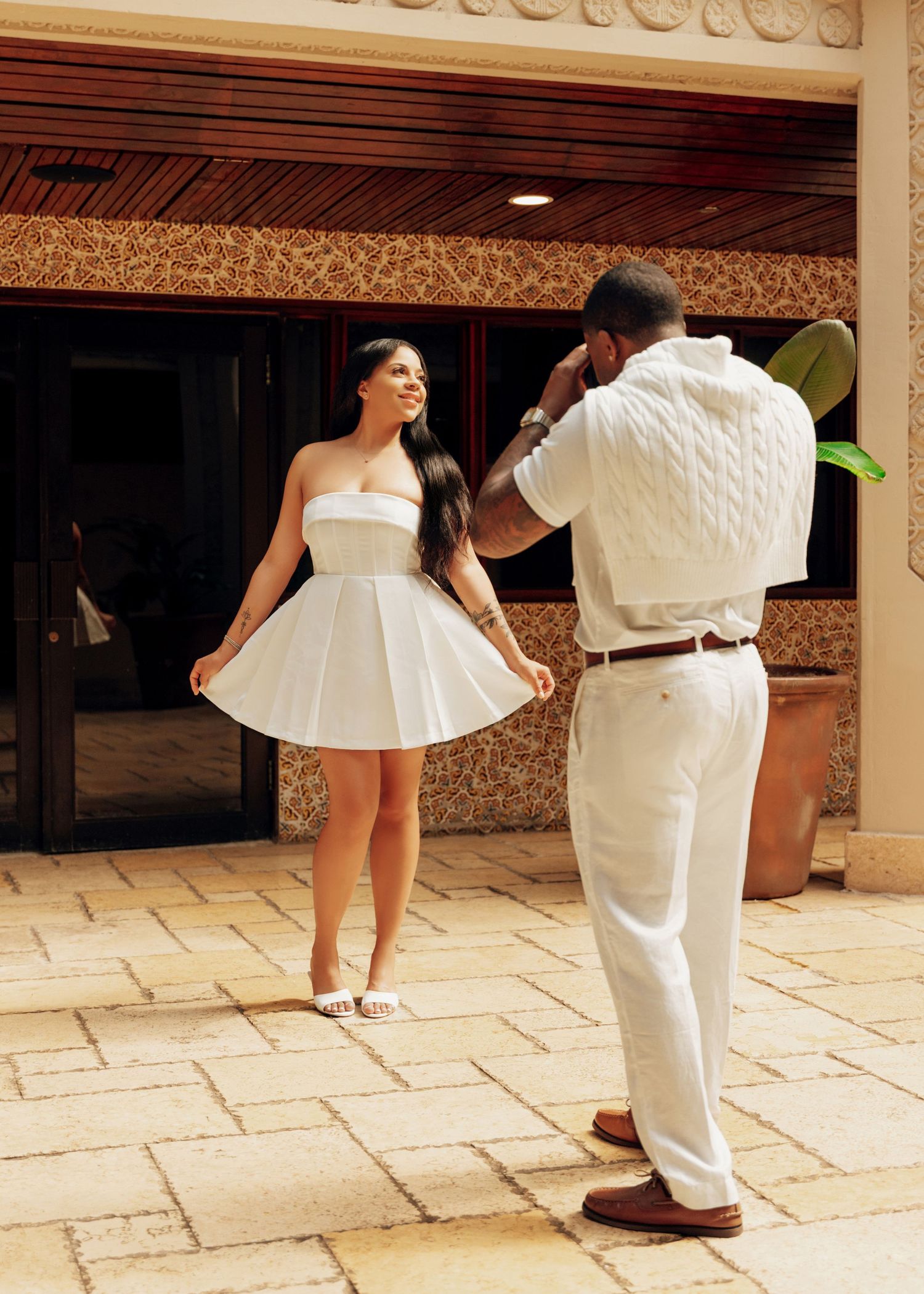 Couple in white outfits dancing and twirling on stone patio.