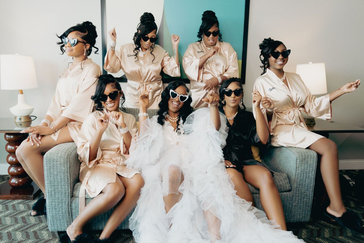 Wedding party relaxes and celebrates together on grey couches during preparation.