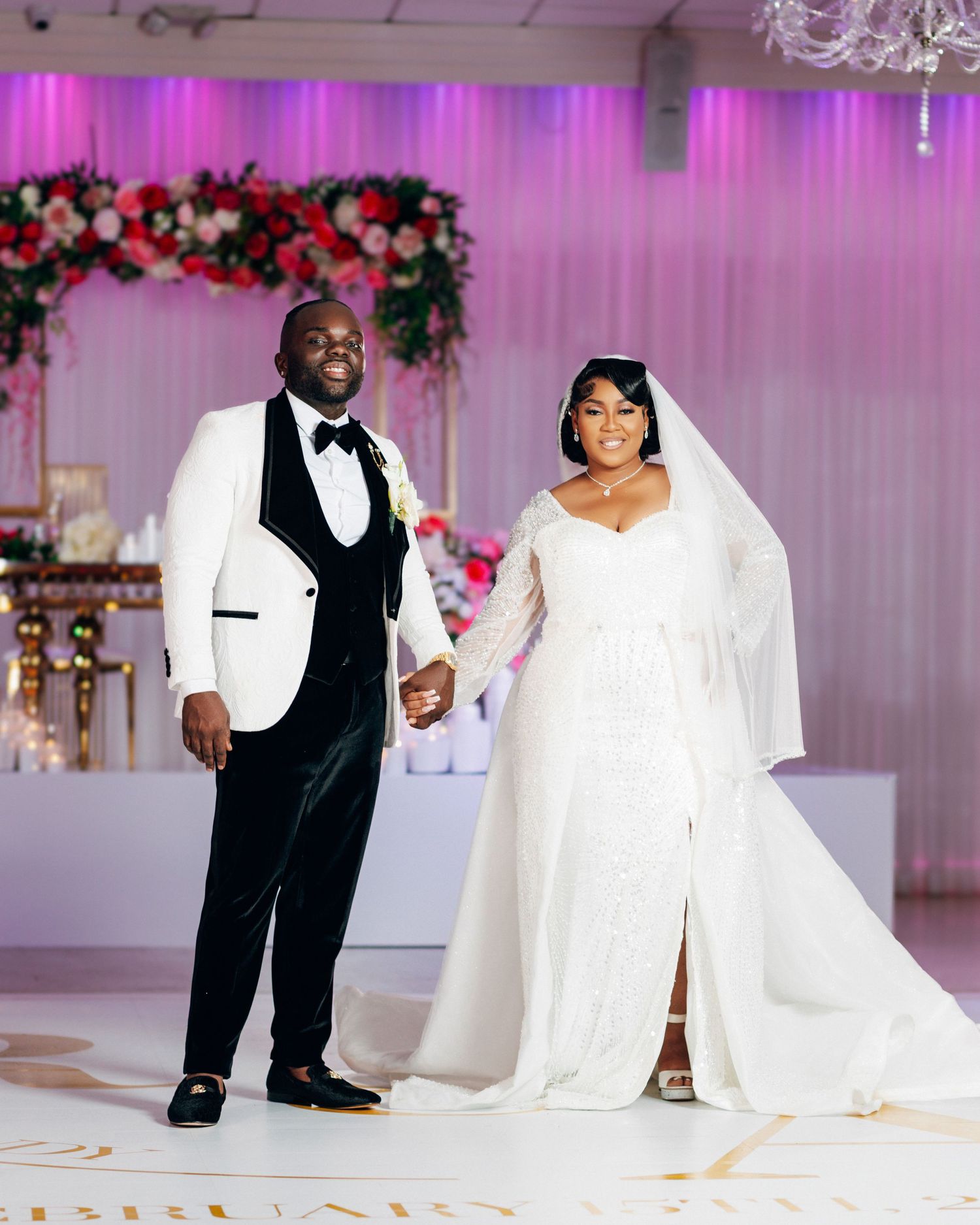 Wedding couple posing in an elegantly decorated reception hall with pink lighting and white draping.