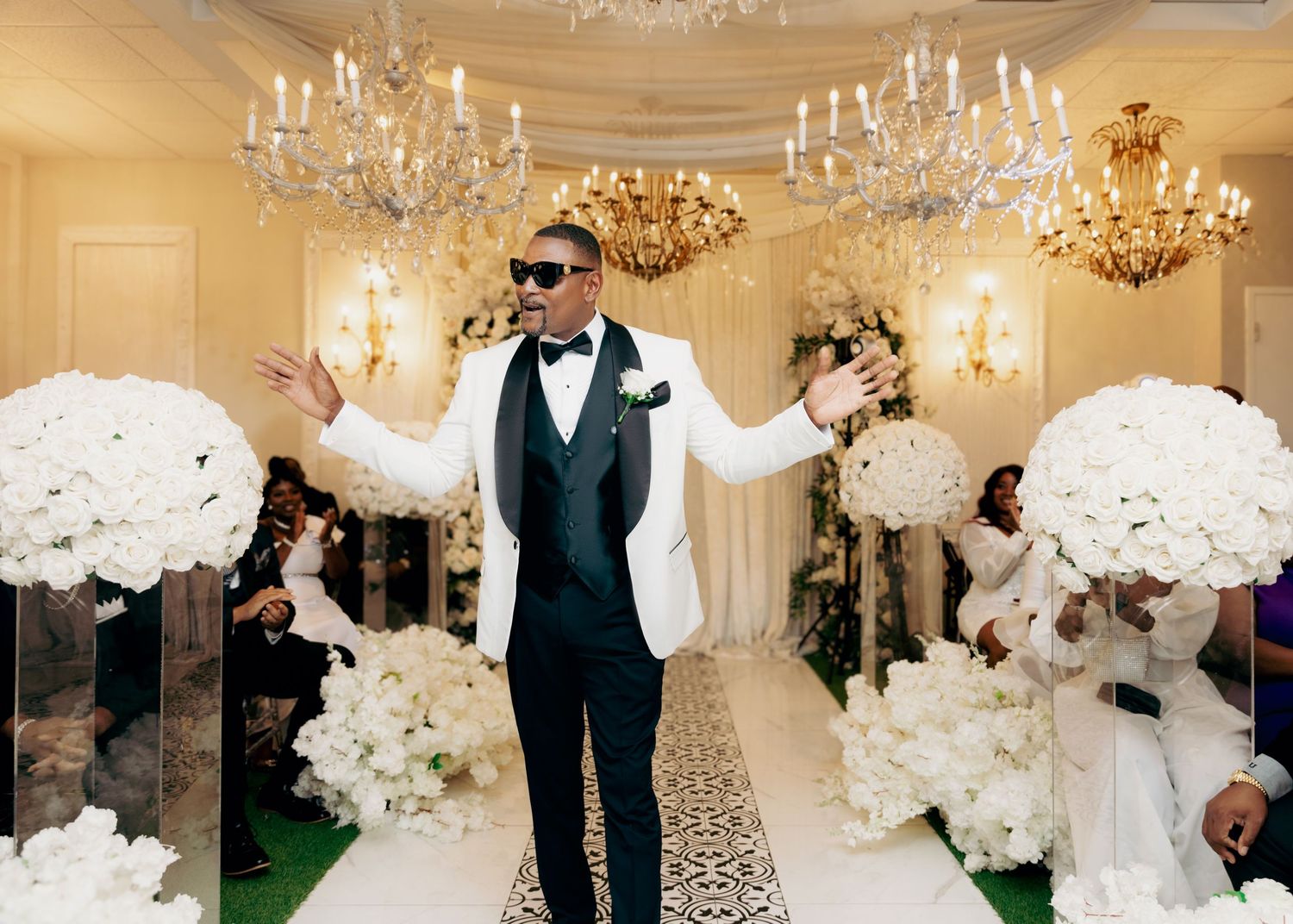 Elegant ballroom wedding ceremony with white floral decorations and crystal chandeliers.
