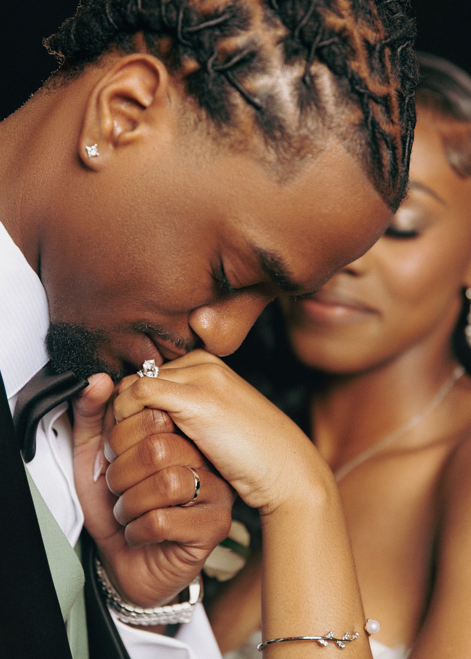 Romantic couple shares an intimate moment as the groom tenderly kisses his bride's hand while wearing formal attire.