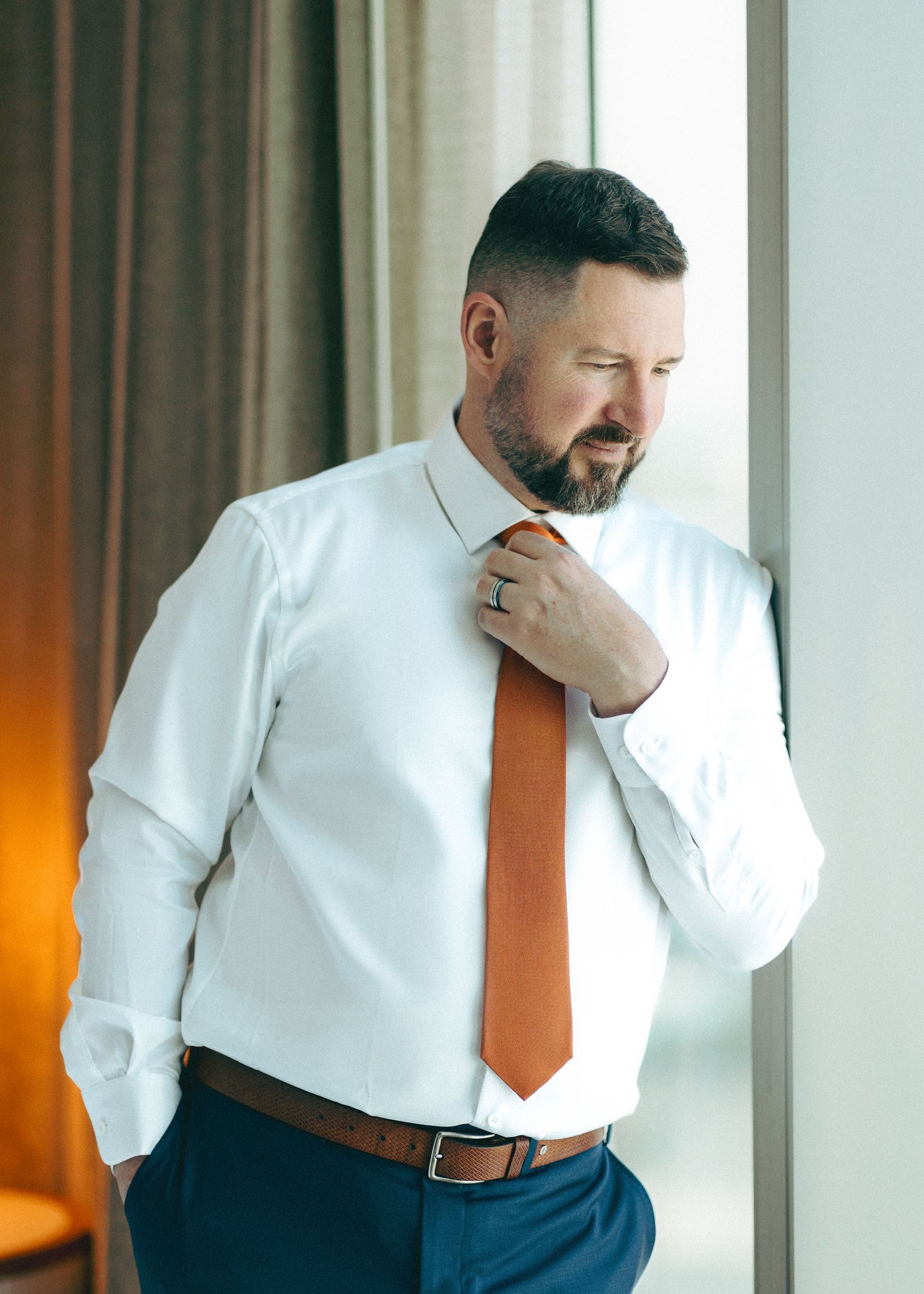 Professional in white shirt and orange tie sneezing into elbow in sequence of five poses by window.