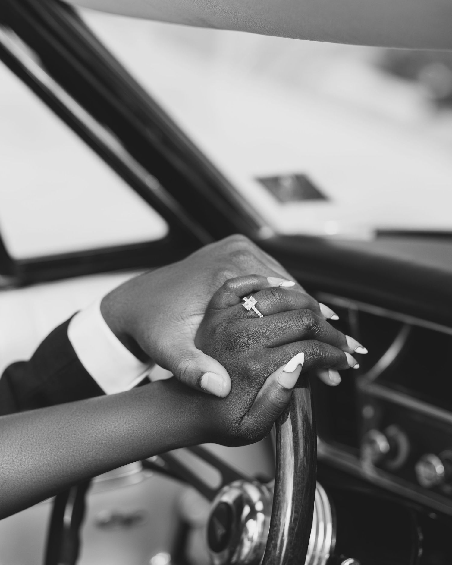 Close-up black and white shots of hands on a steering wheel showing an engagement ring.