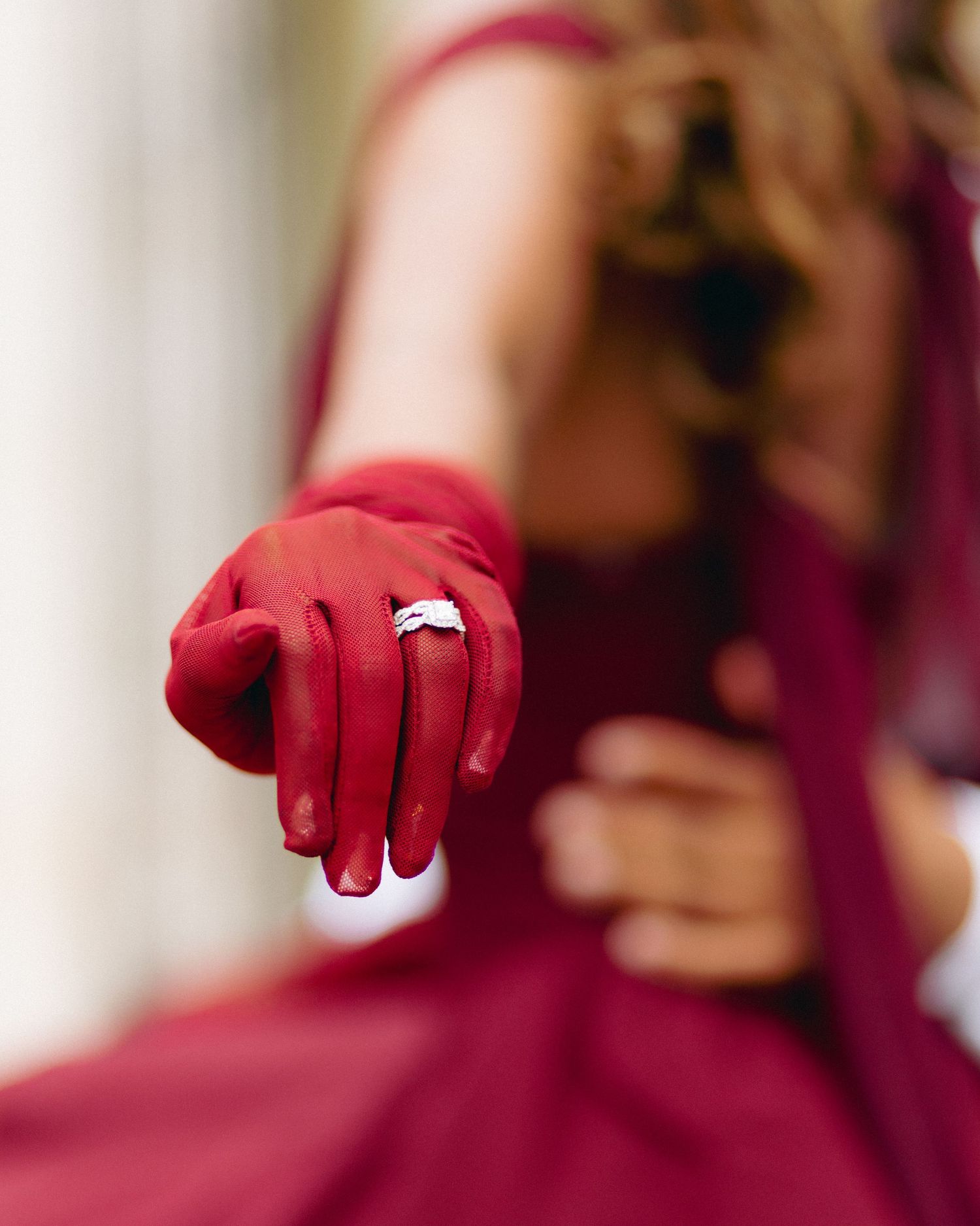 Close-up view of hands wearing bright red gloves against a blurred burgundy background.