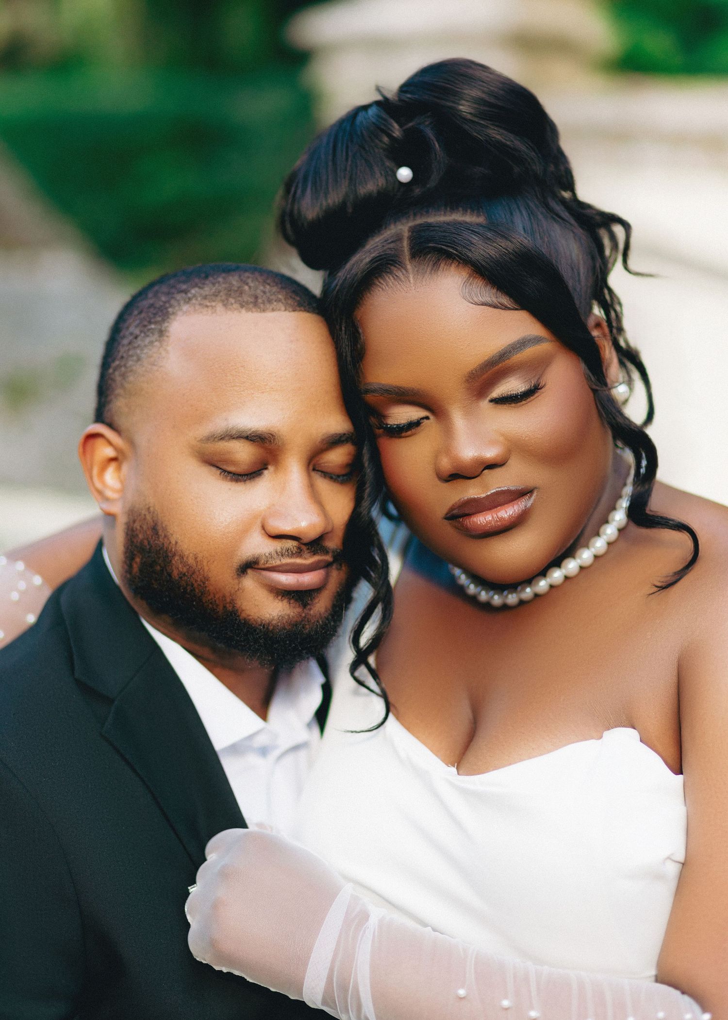 Elegant bride and groom in wedding attire share a tender romantic moment, bride wearing pearl necklace and updo hairstyle.