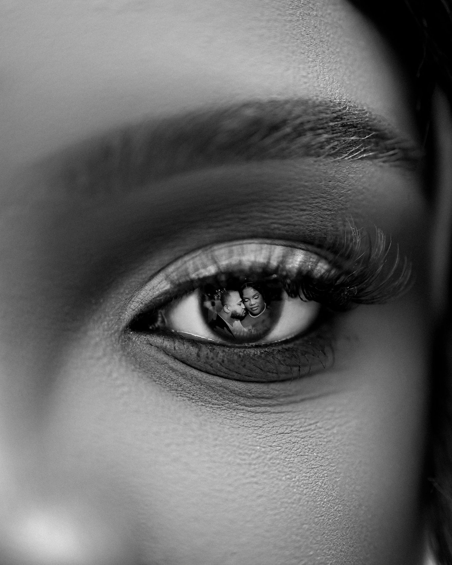 Close-up black and white macro photo of a womans eye with long lashes and a reflection visible in the iris.