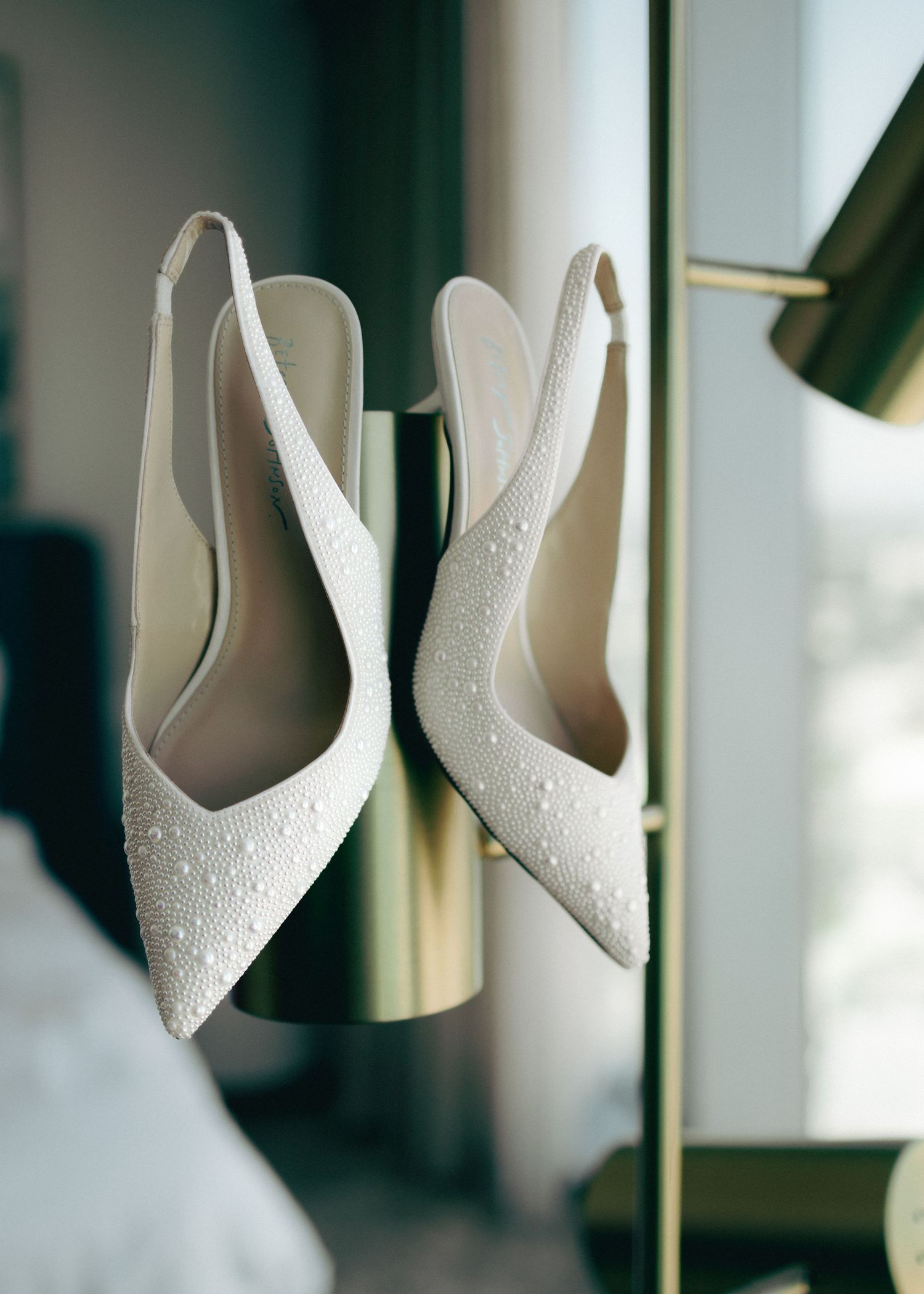 White beaded bridal shoes arranged in a row on a glass shelf with soft lighting and reflections.