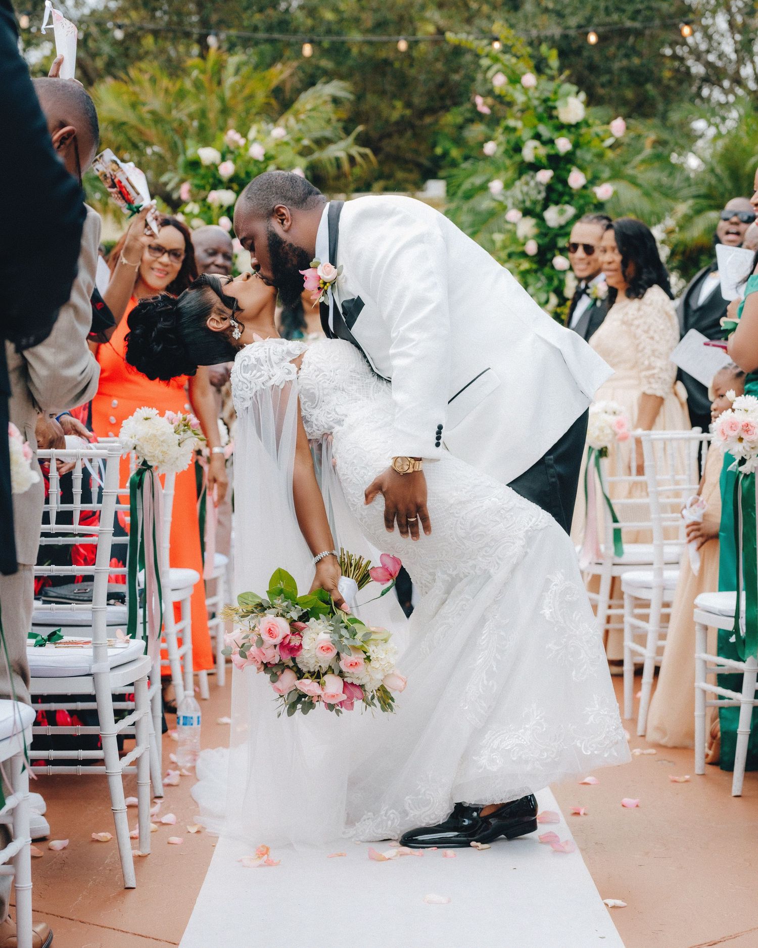 Wedding guests dancing and celebrating on an outdoor terrace with white chairs.