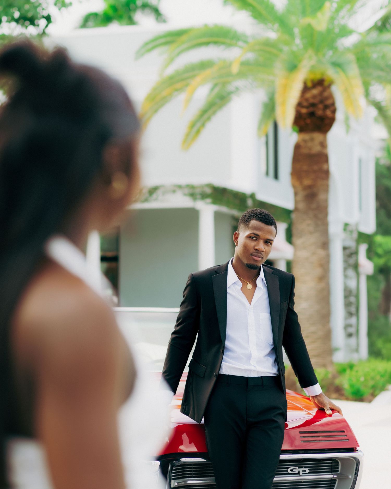 Elegant photoshoot with palm trees and a classic red car as backdrop.