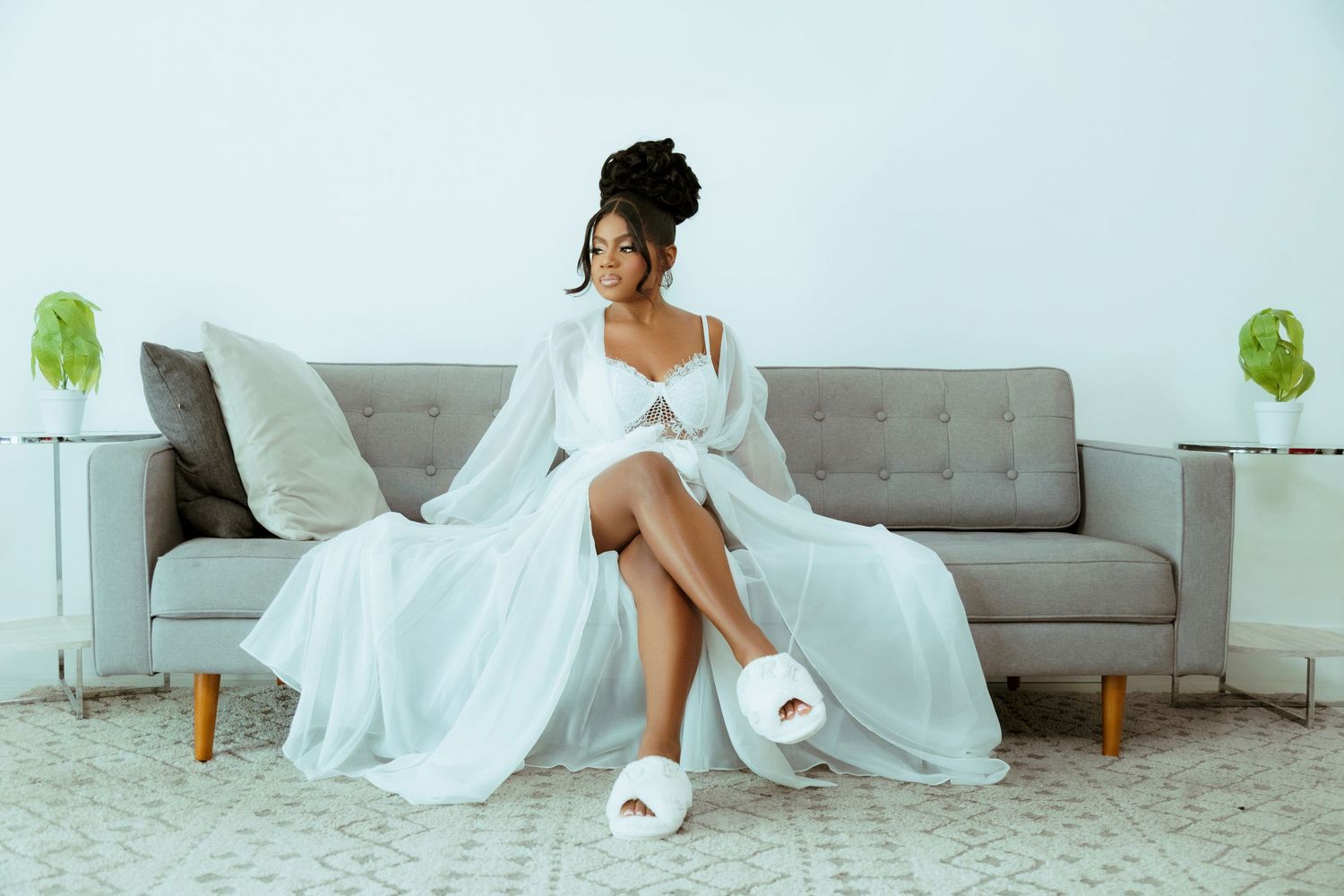 Bride in white dress posing gracefully on modern grey couch.