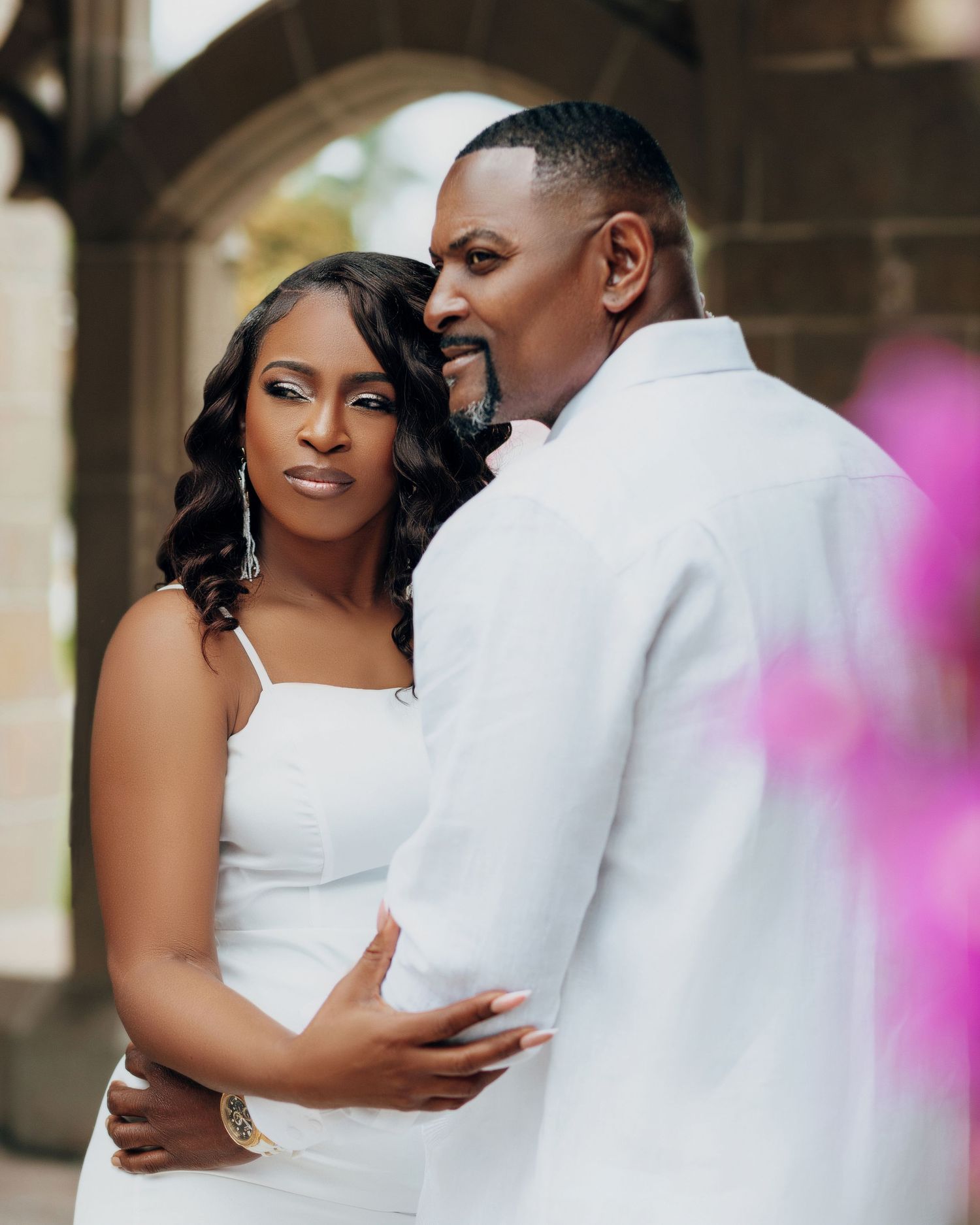 Wedding couple embracing in front of stone architecture with pink floral accents.
