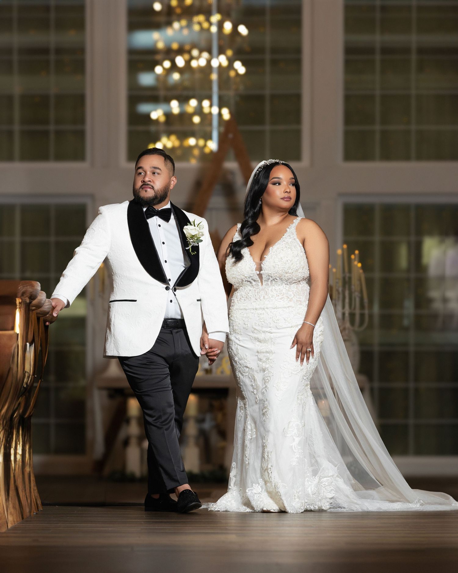Romantic wedding couple poses in elegant ballroom with chandeliers and large windows.